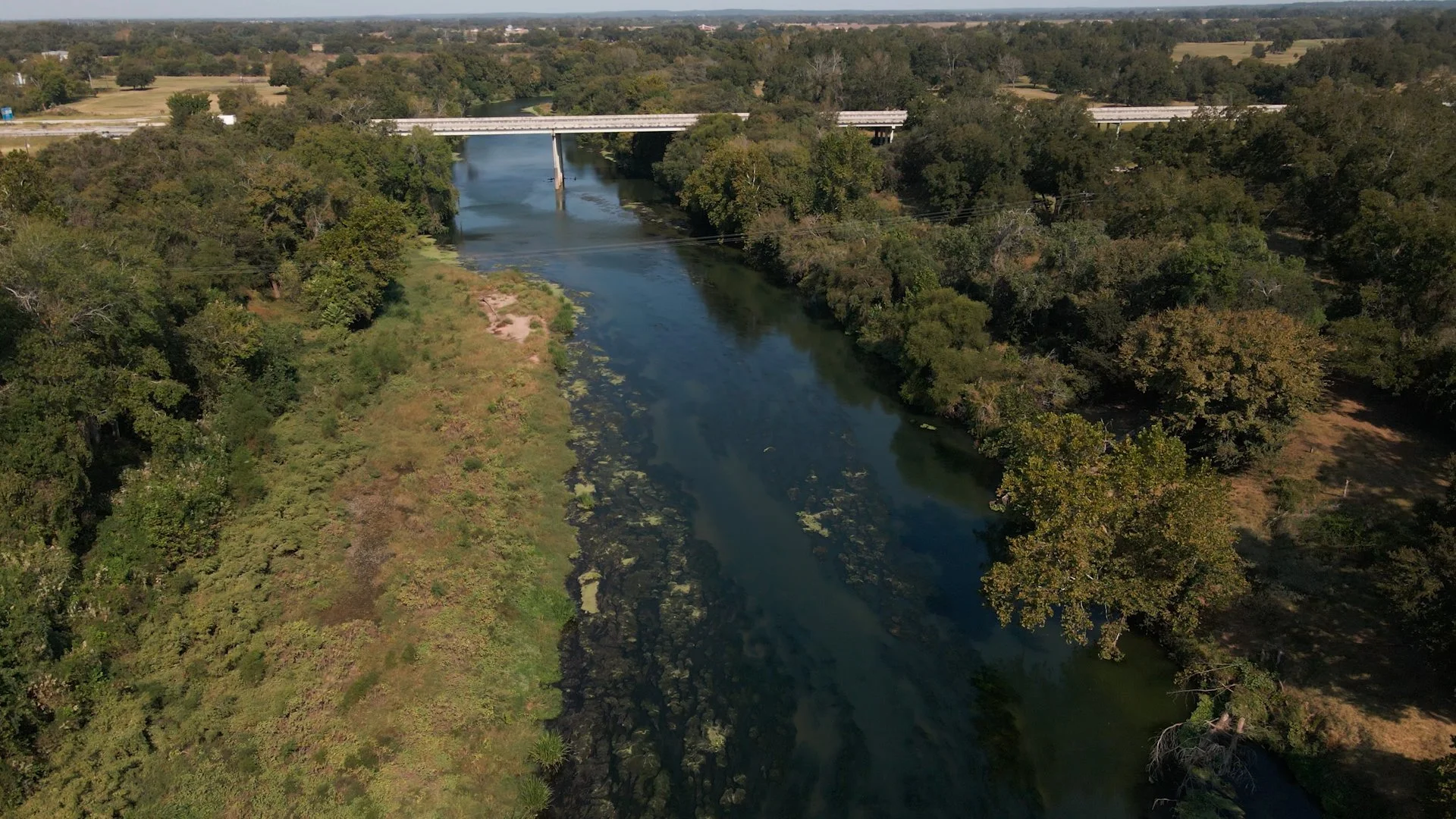 Aerial view of a river running through a green landscape with trees on both sides, and a bridge crossing over the river.