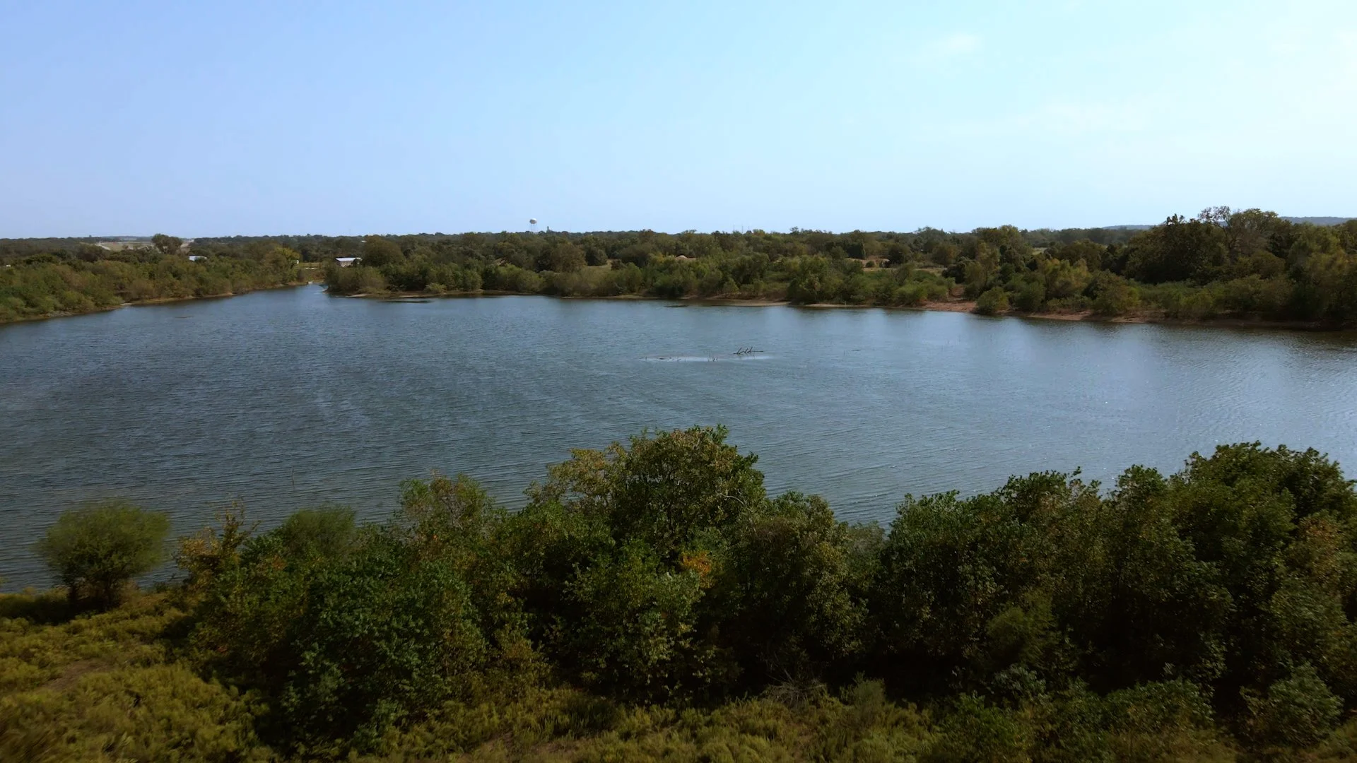 A large body of water surrounded by trees, with clear skies overhead.