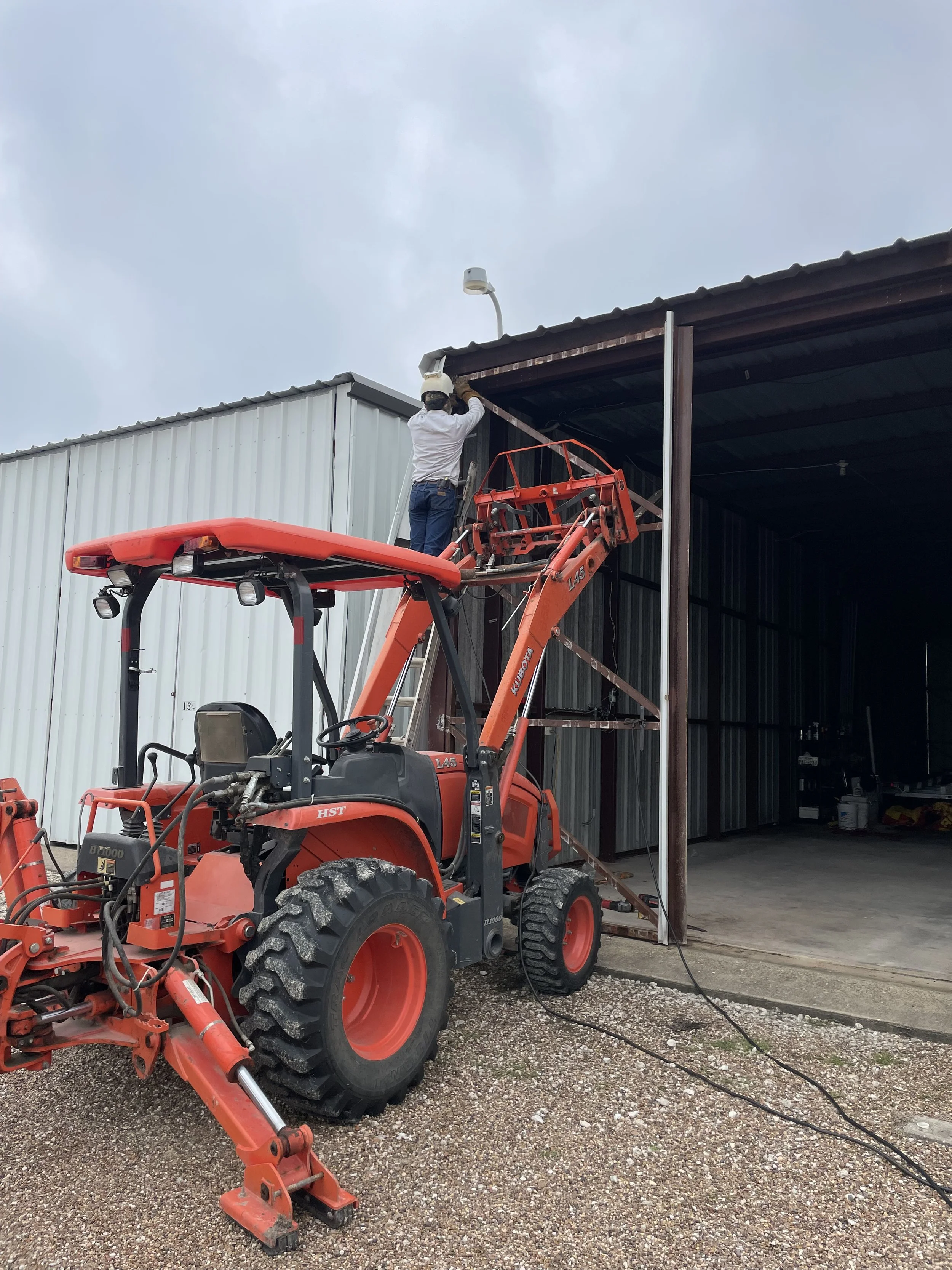 A worker in safety gear on a lift doing maintenance on a security camera on an outdoor building.