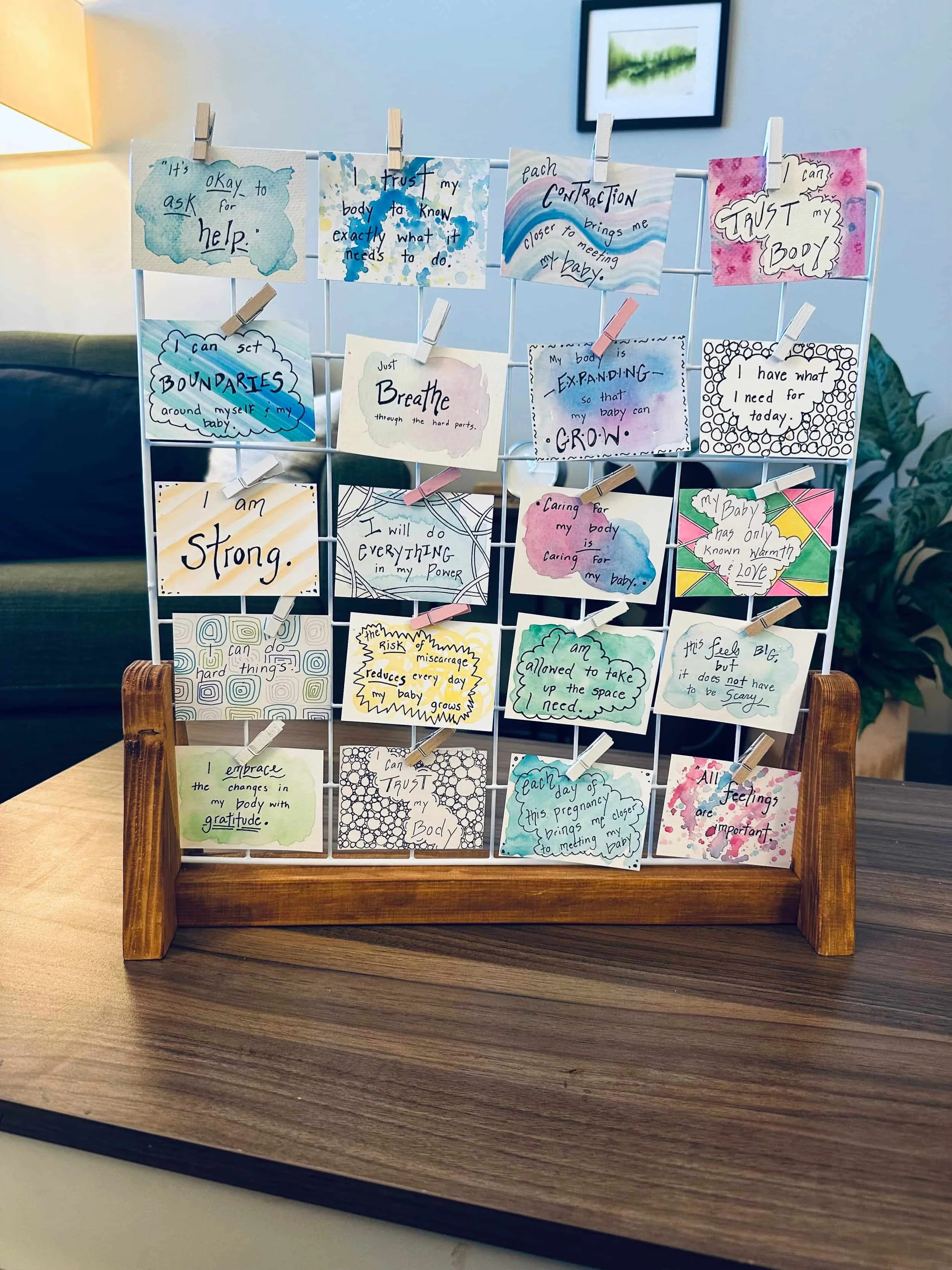 A wooden stand holds colorful, handwritten affirmation cards, each with positive messages, displayed on a metal grid in a cozy  therapy office