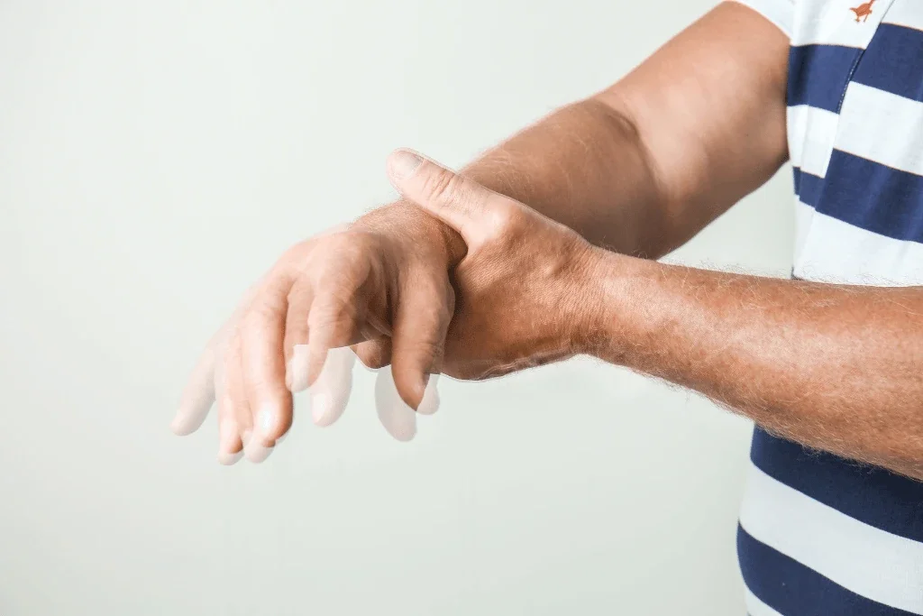 A person wearing a striped shirt is holding their wrist with one hand, possibly checking or massaging it.