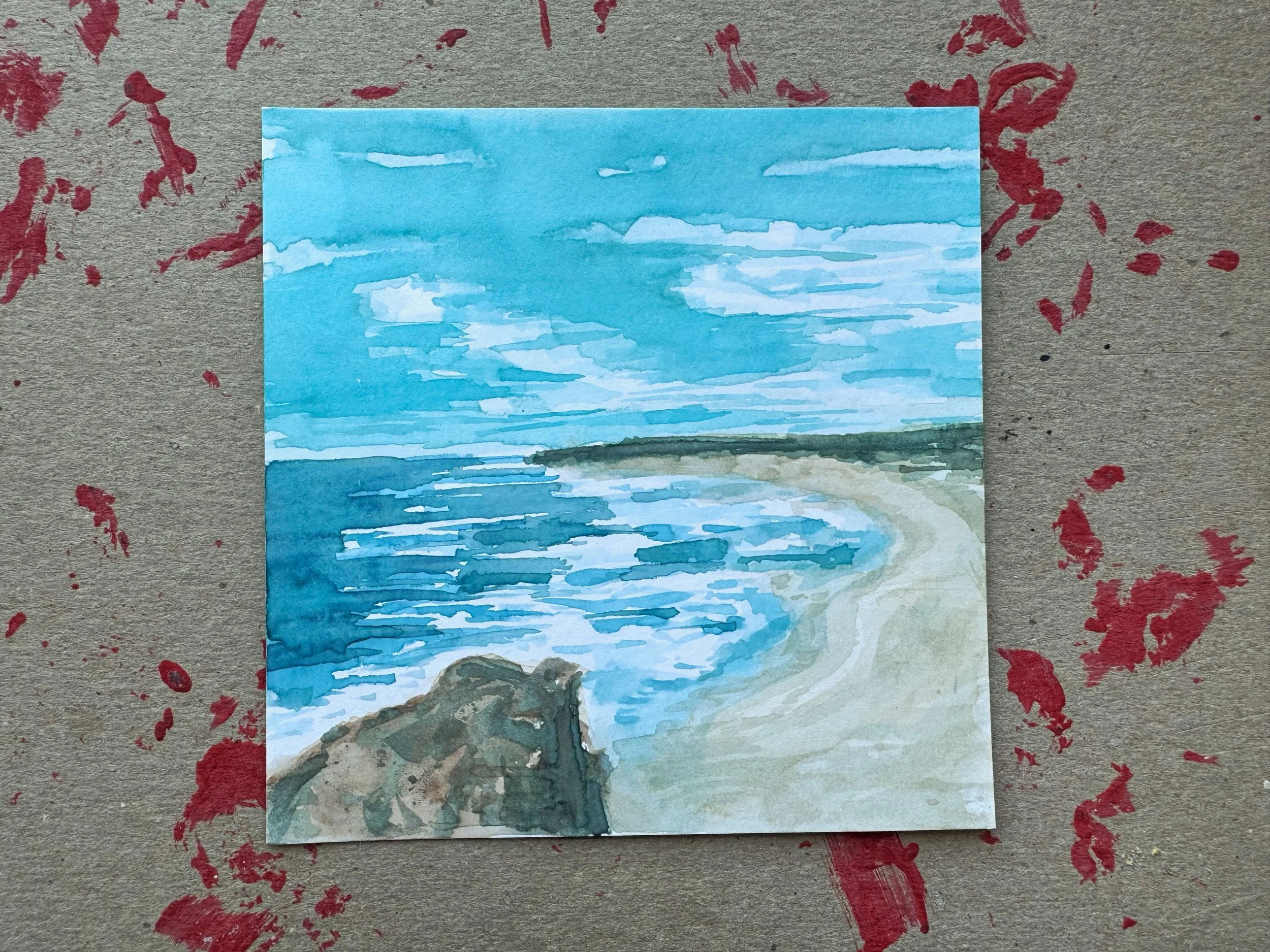 A watercolor painting of a beach with ocean waves, a sandy shoreline, and a cloudy sky. There are some rocks in the foreground and a distant green shoreline across the water.