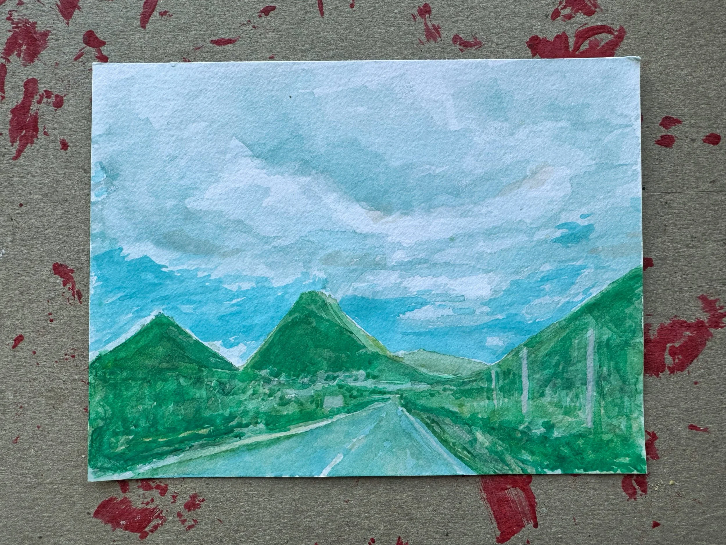 Watercolor painting of a mountain landscape with a road running through green mountains under a cloudy sky.