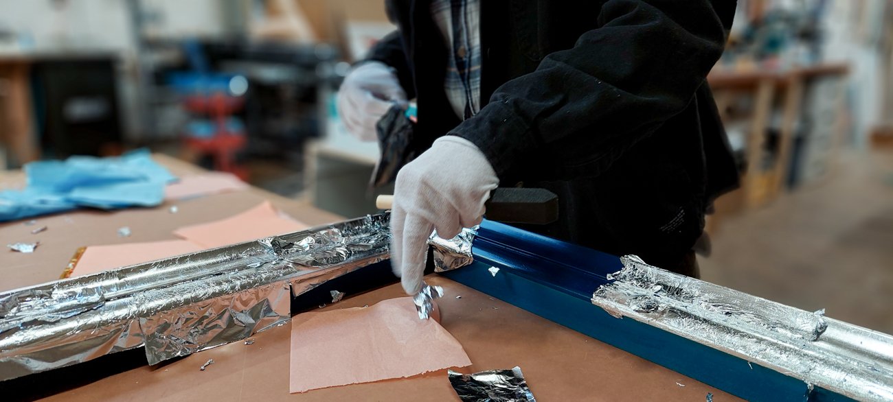 Gloved fabricator applies silver leaf
