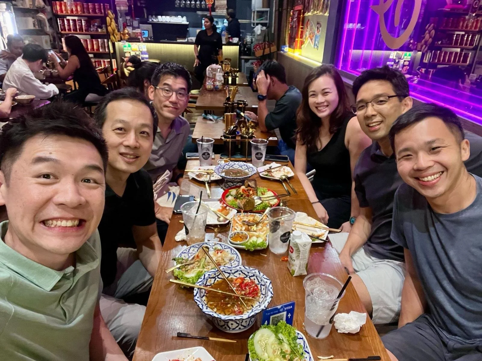 Group of friends celebrating at a restaurant with food and drinks on the table, smiling for the camera.