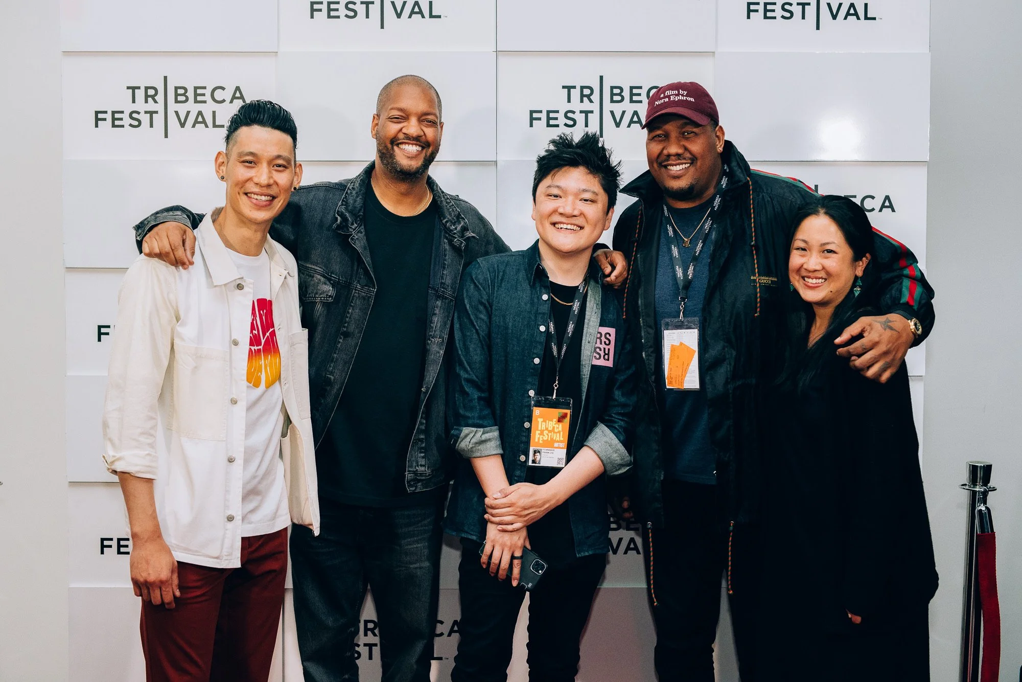 Group of five diverse people smiling and standing together at Tribeca Festival, with a backdrop displaying Tribeca Festival signage.
