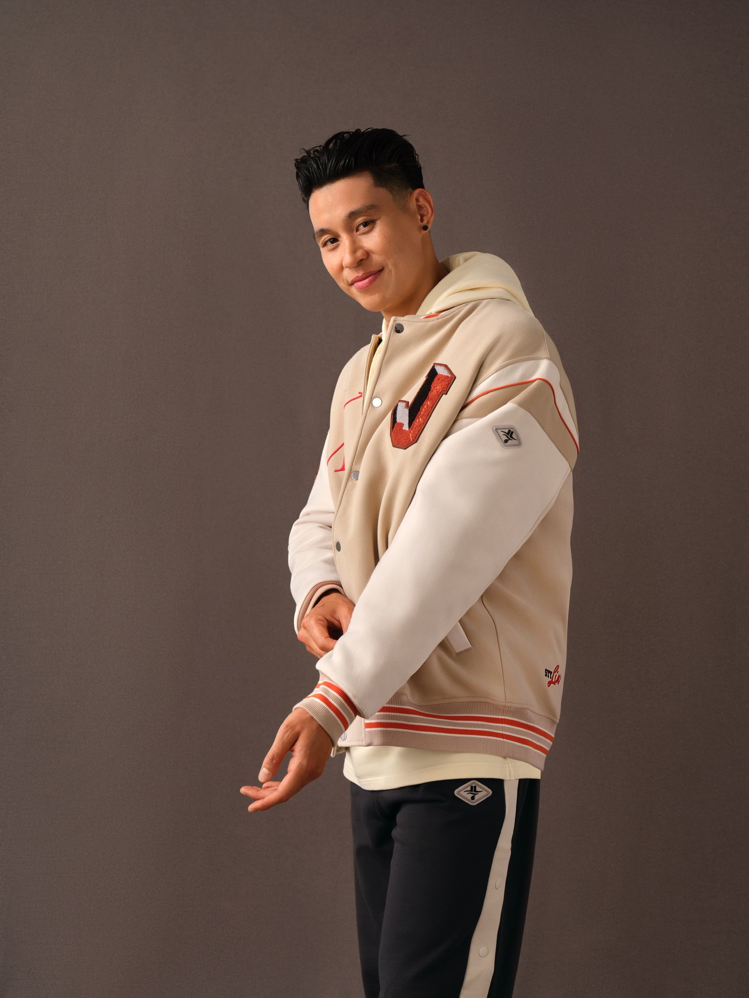 Person wearing a beige and white varsity jacket with red accents, standing against a neutral background.