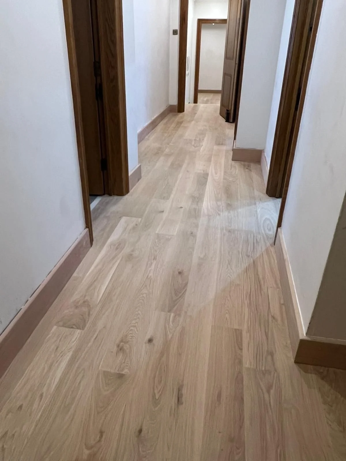 Wooden hallway with light-colored hardwood flooring and door frames.