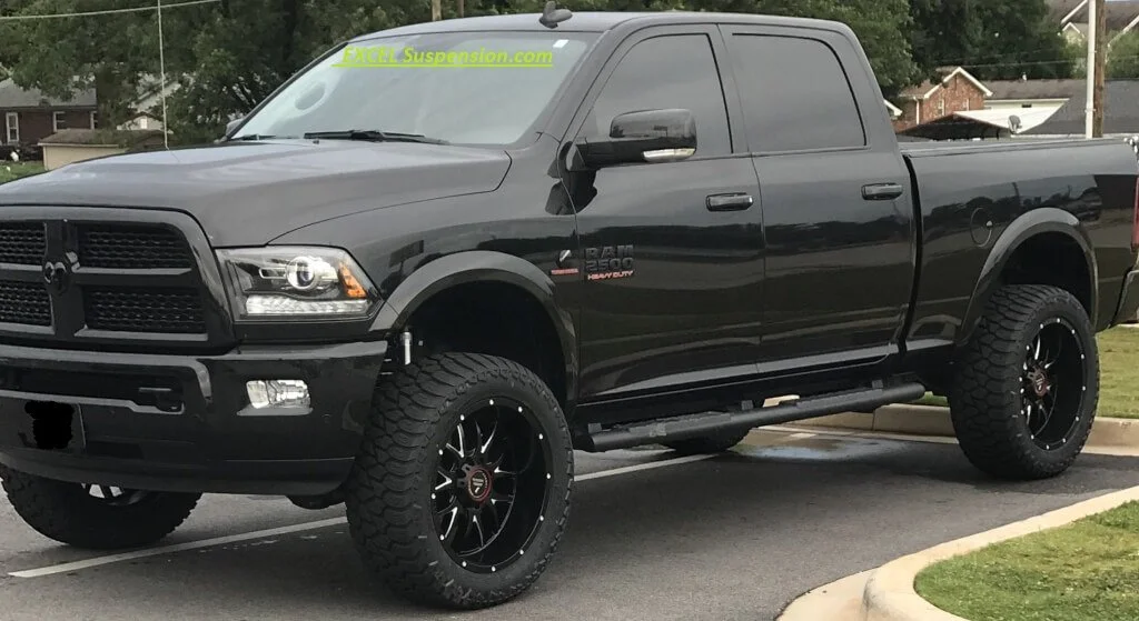 Black RAM 1500 pickup truck with large tires and aftermarket rims parked in a parking lot.