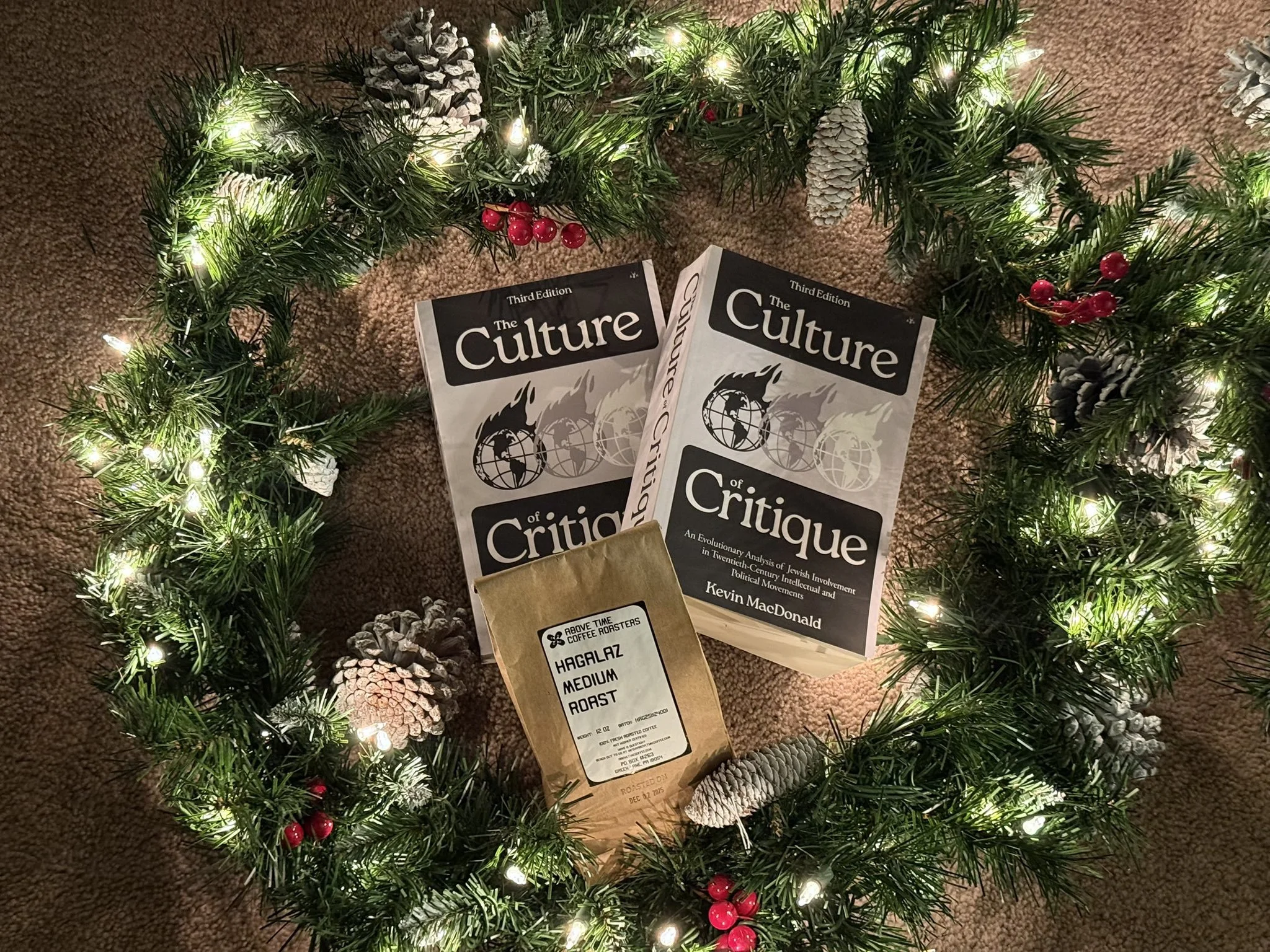 Books titled 'The Culture of Critique' surrounded by Christmas greenery with pinecones and red berries, on a brown carpet.