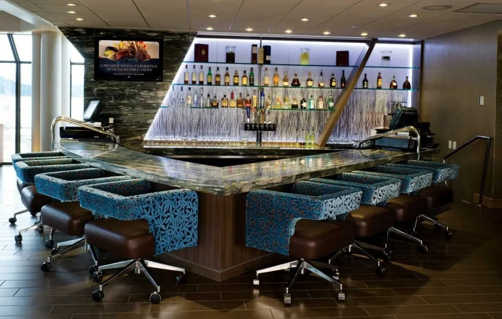 Upscale hotel bar with a marble counter, blue patterned chairs, and a backlit display of liquor bottles.