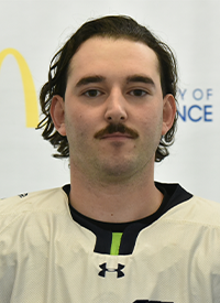 Portrait of a man with a beard wearing a gray blazer and dark shirt.