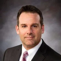 Man in a suit posing for a professional portrait against a gray background.