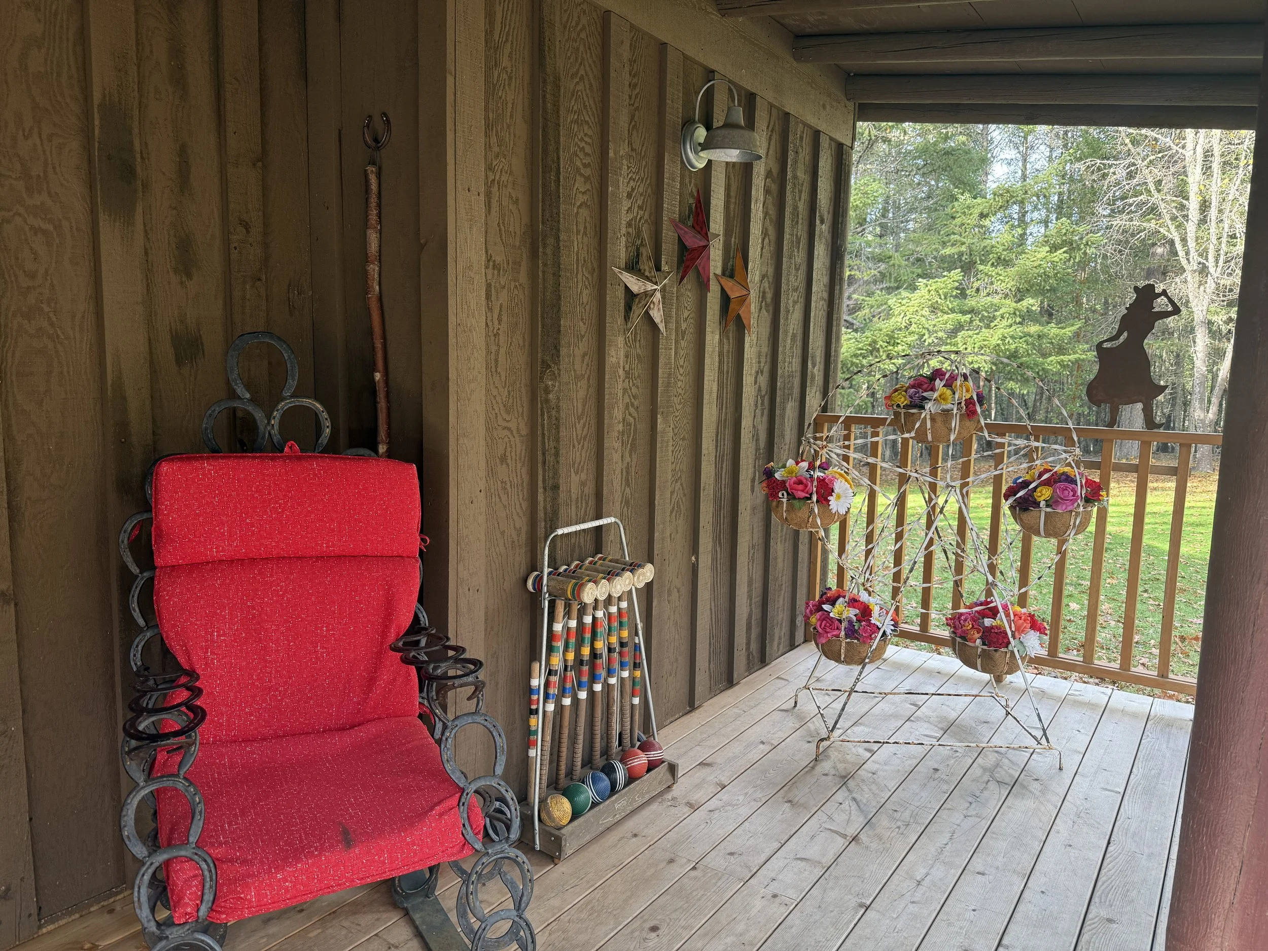 Rustic porch with a vibrant red rocking chair, decorative flower display, and vintage croquet set overlooking peaceful forest views.