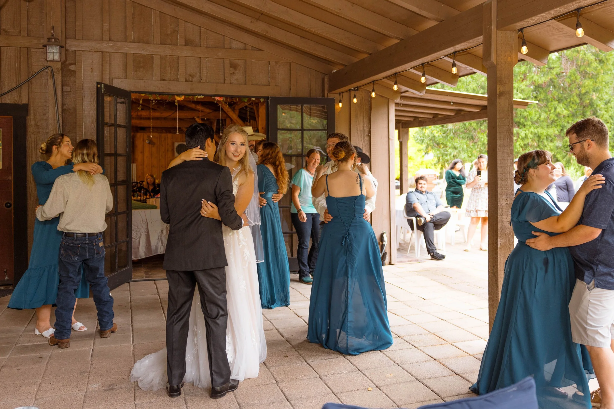 Couple dancing at a wedding reception outdoors, with guests socializing and taking photos in the background.