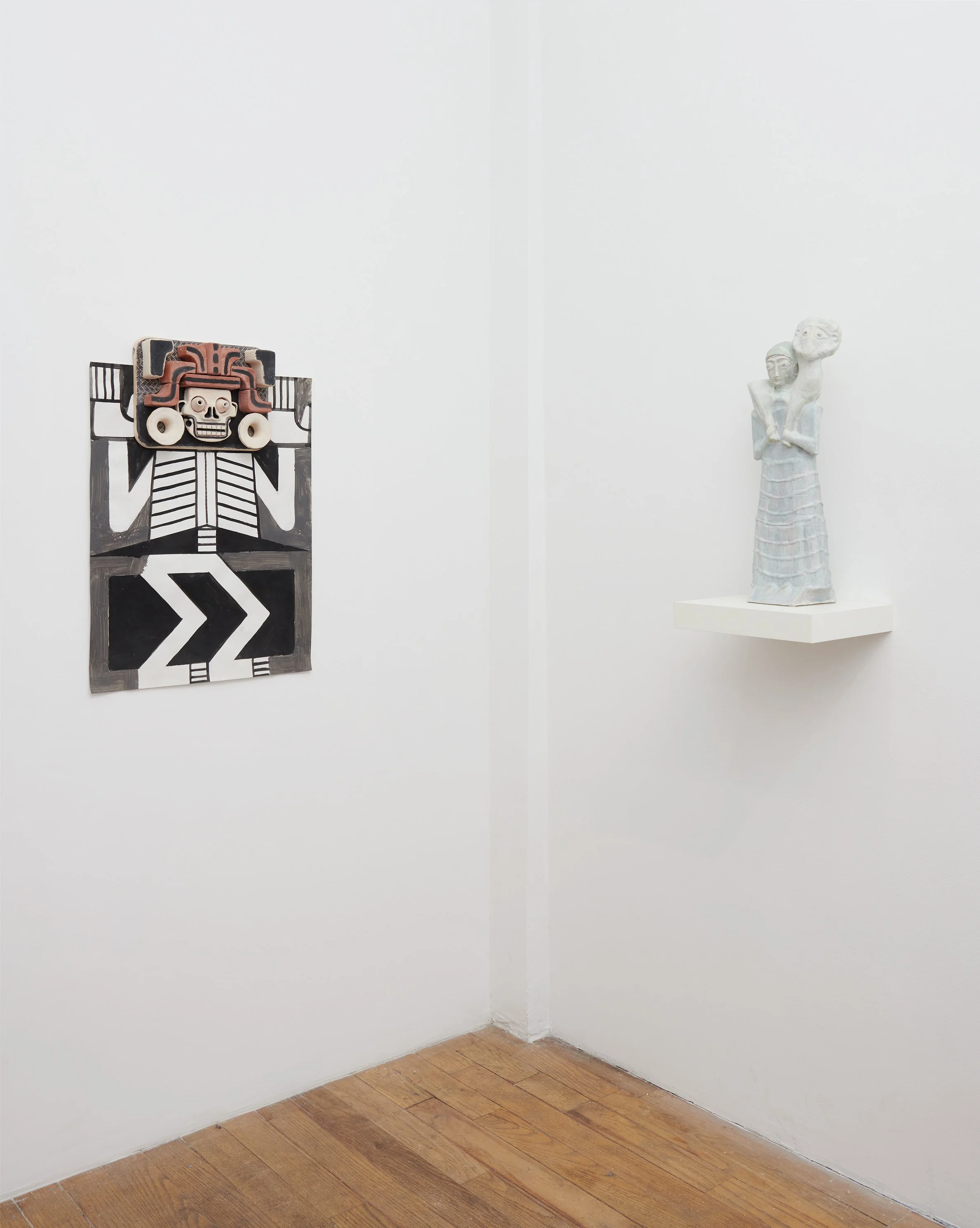  A photograph of a&nbsp;vertical ceramic artwork by Steve Keister mounted on a white gallery wall and a&nbsp;20 and a half by 8 by 5 inch contemporary mixed-media sculpture by Shari Mendelson titled Ram Bearer, crafted from repurposed plastic. 