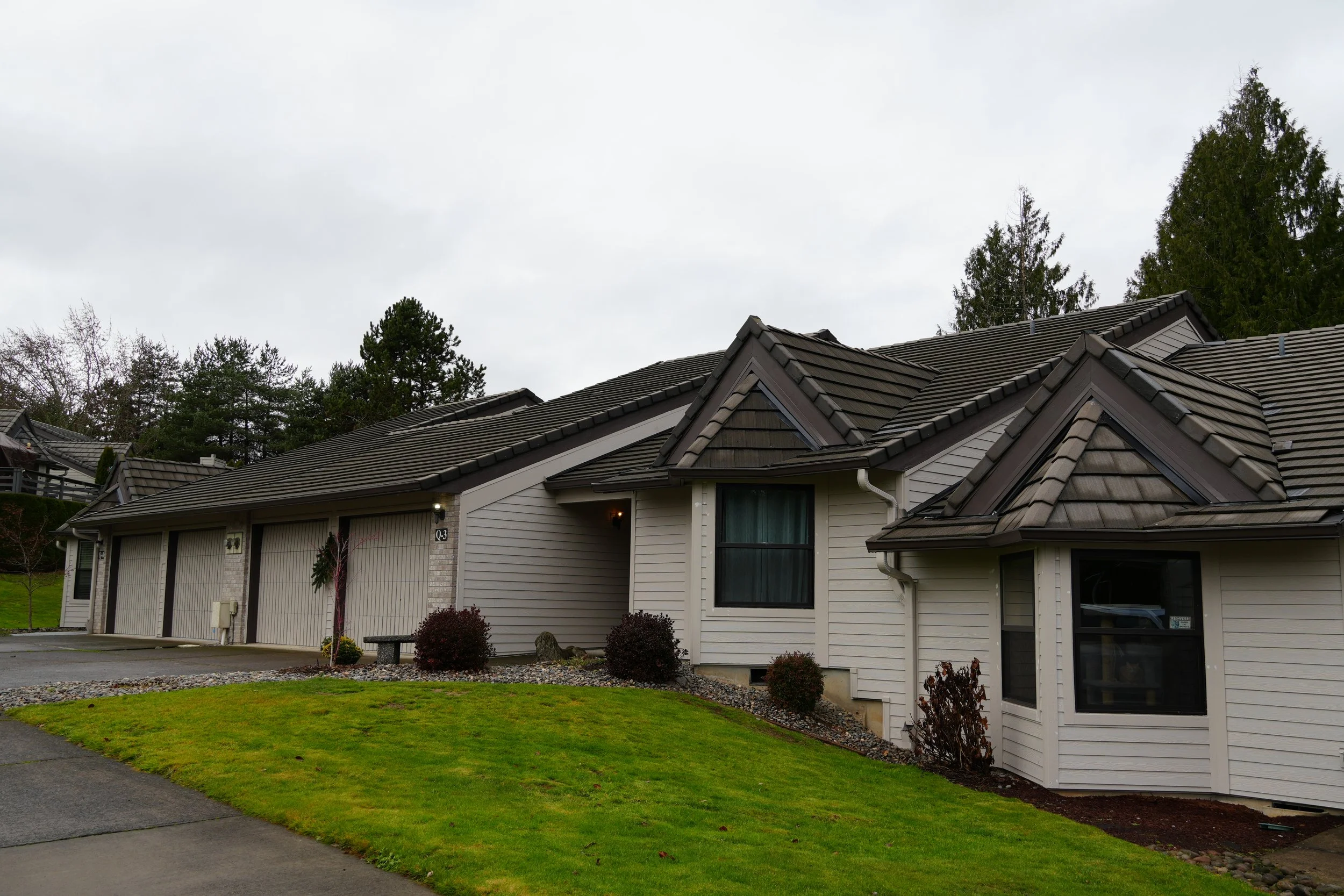 Residential house with gray siding and tiled roof, surrounded by lawn and trees.