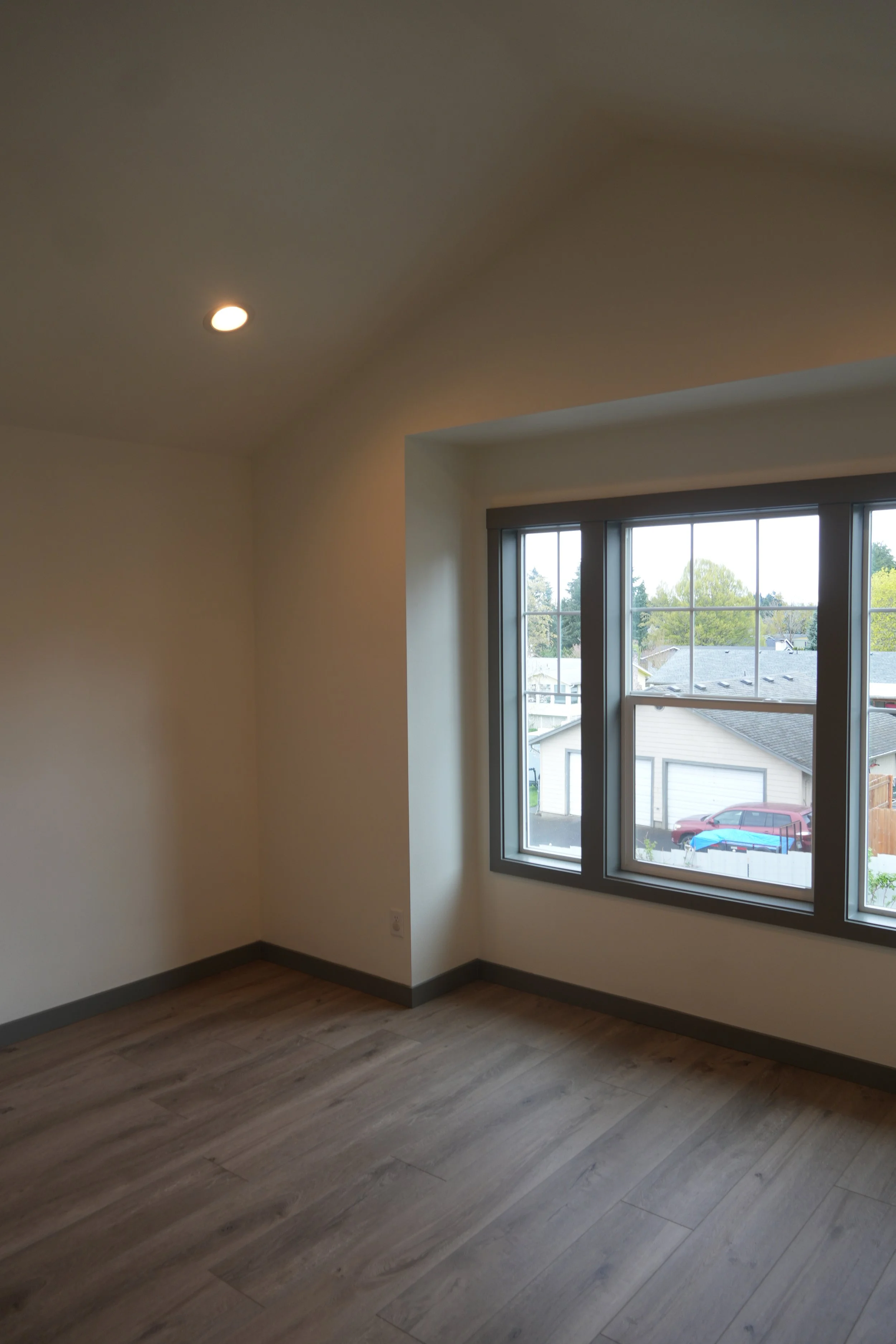 Empty room with large window, beige walls, and wood flooring.