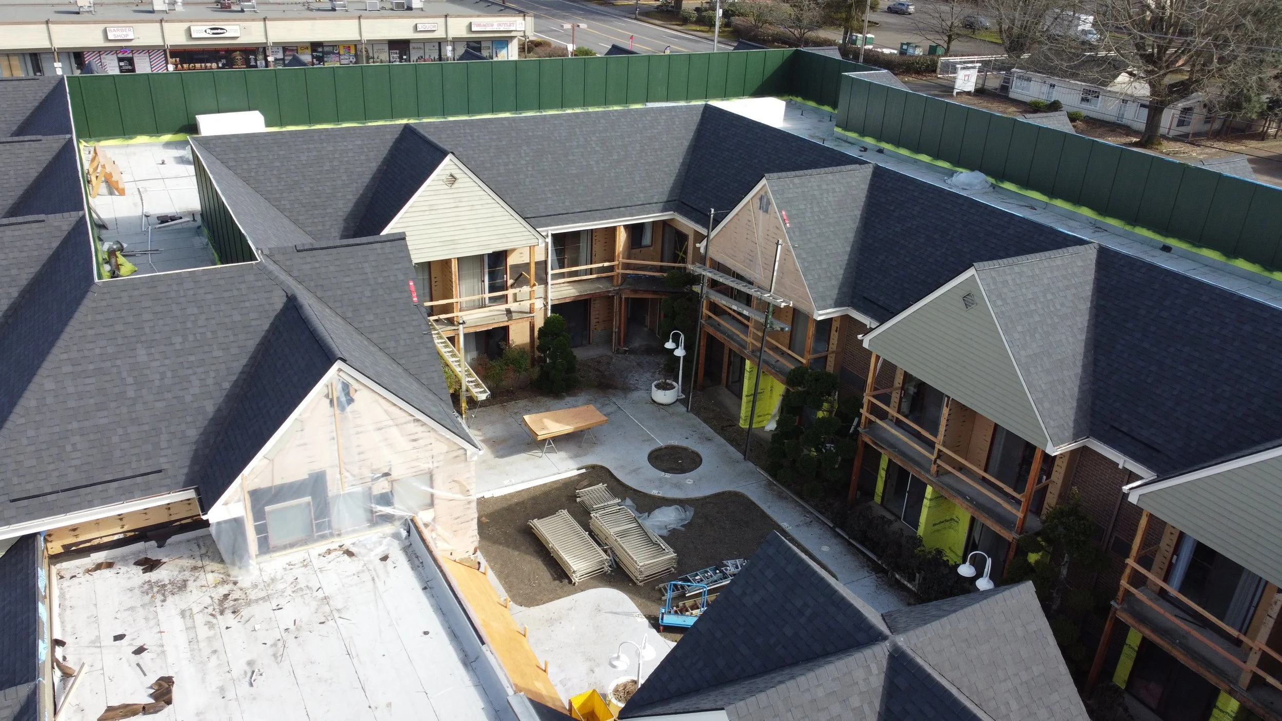 Aerial view of a multi-unit residential apartment complex under construction, with gray shingle roofs, scaffolding, construction materials, and a courtyard area.