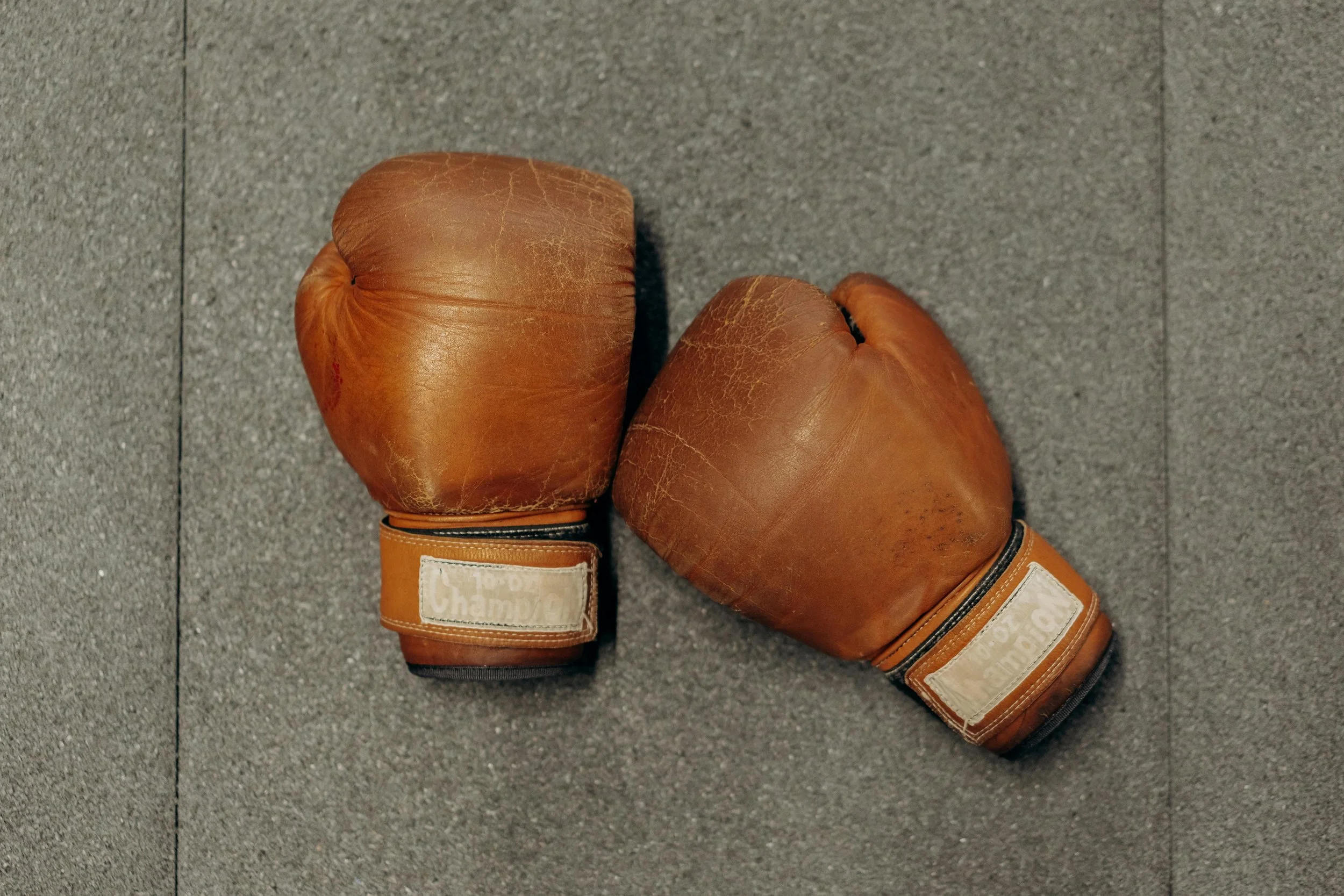 A pair of vintage brown leather boxing gloves placed on a gray surface.