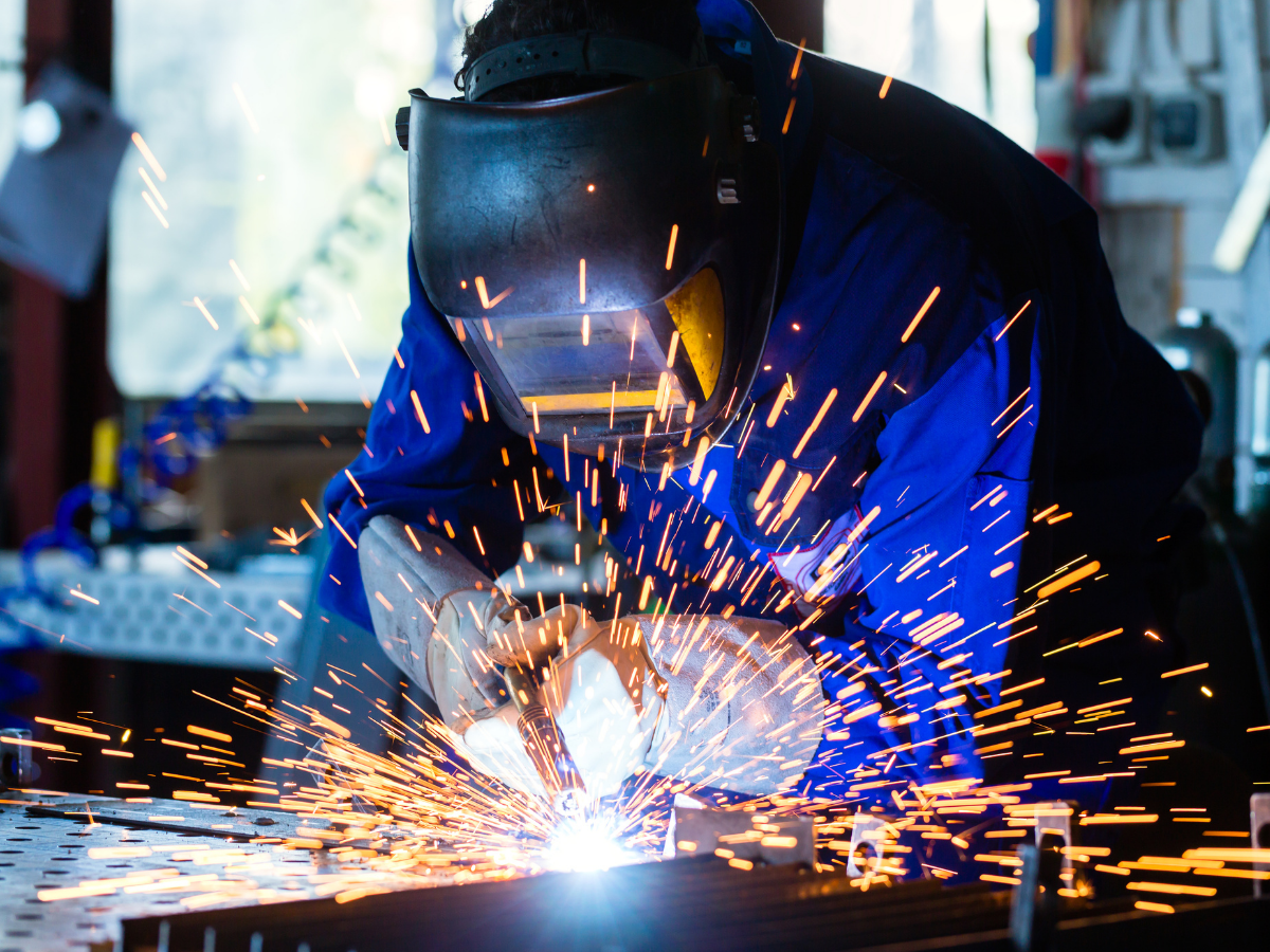 A welder wearing safety gear welding metal, with sparks flying in a workshop.