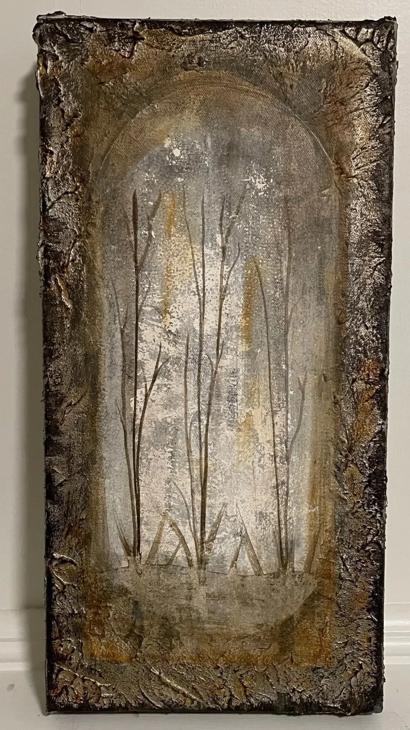 A textured vertical wall art piece with a metallic finish, depicting delicate plant stems and leaves within an oval frame.