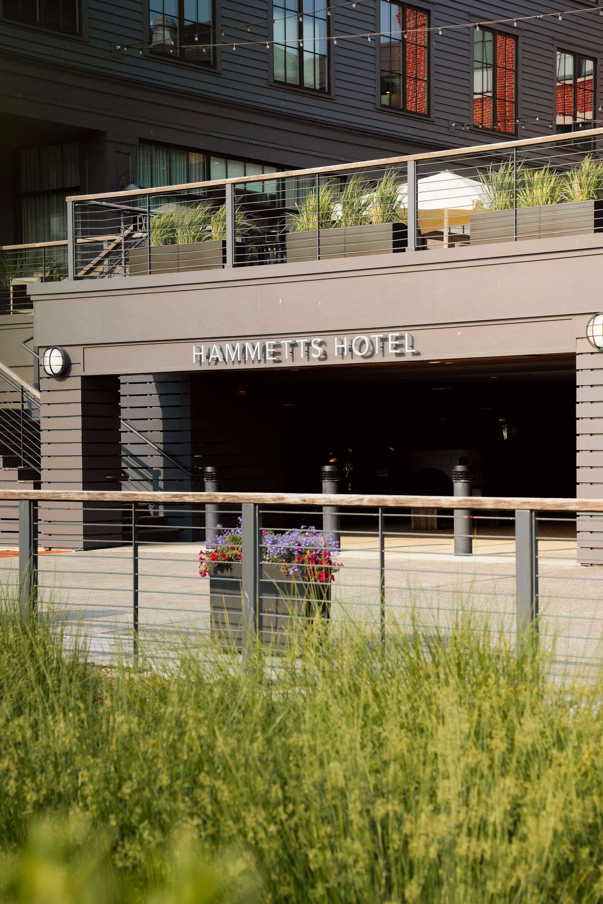 Exterior view of the Hammetts Hotel with a parking entrance, plant pots with flowers, and a balcony with greenery in a city setting.
