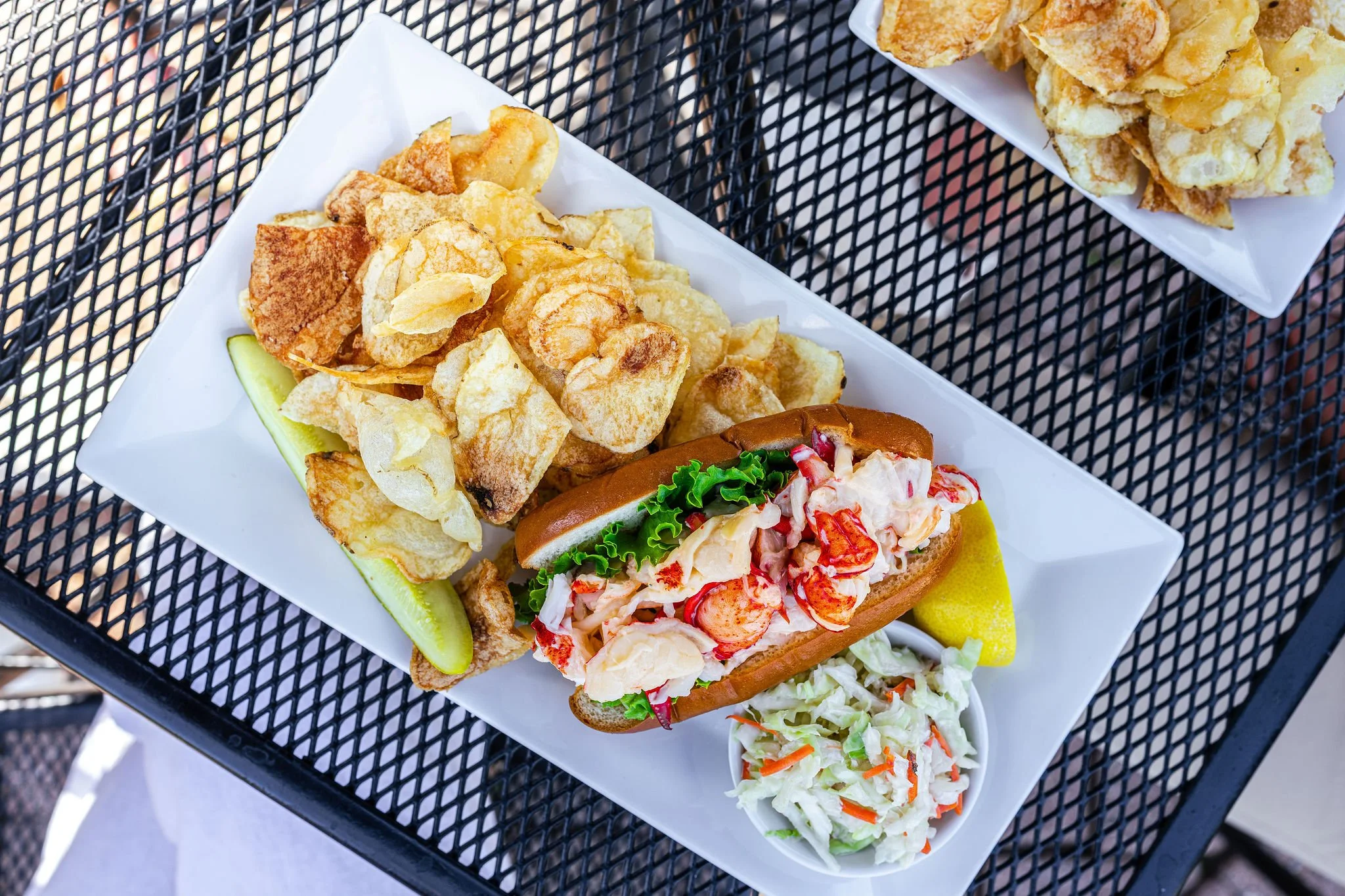 Lobster roll, potato chips, coleslaw, and a lemon wedge on a white plate