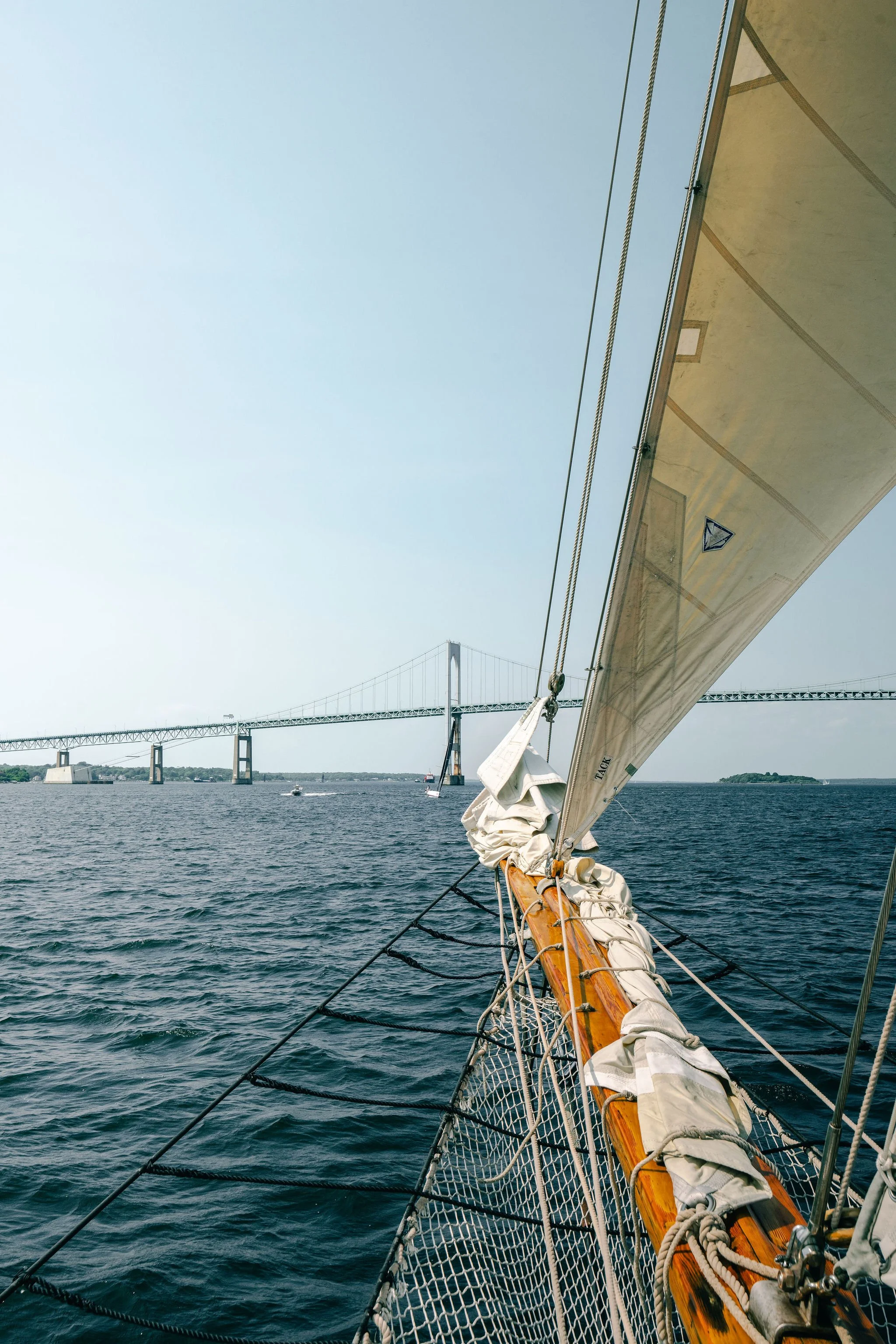 View from a sailboat on the water with a bridge in the distance, the boat's sail and rigging in the foreground.