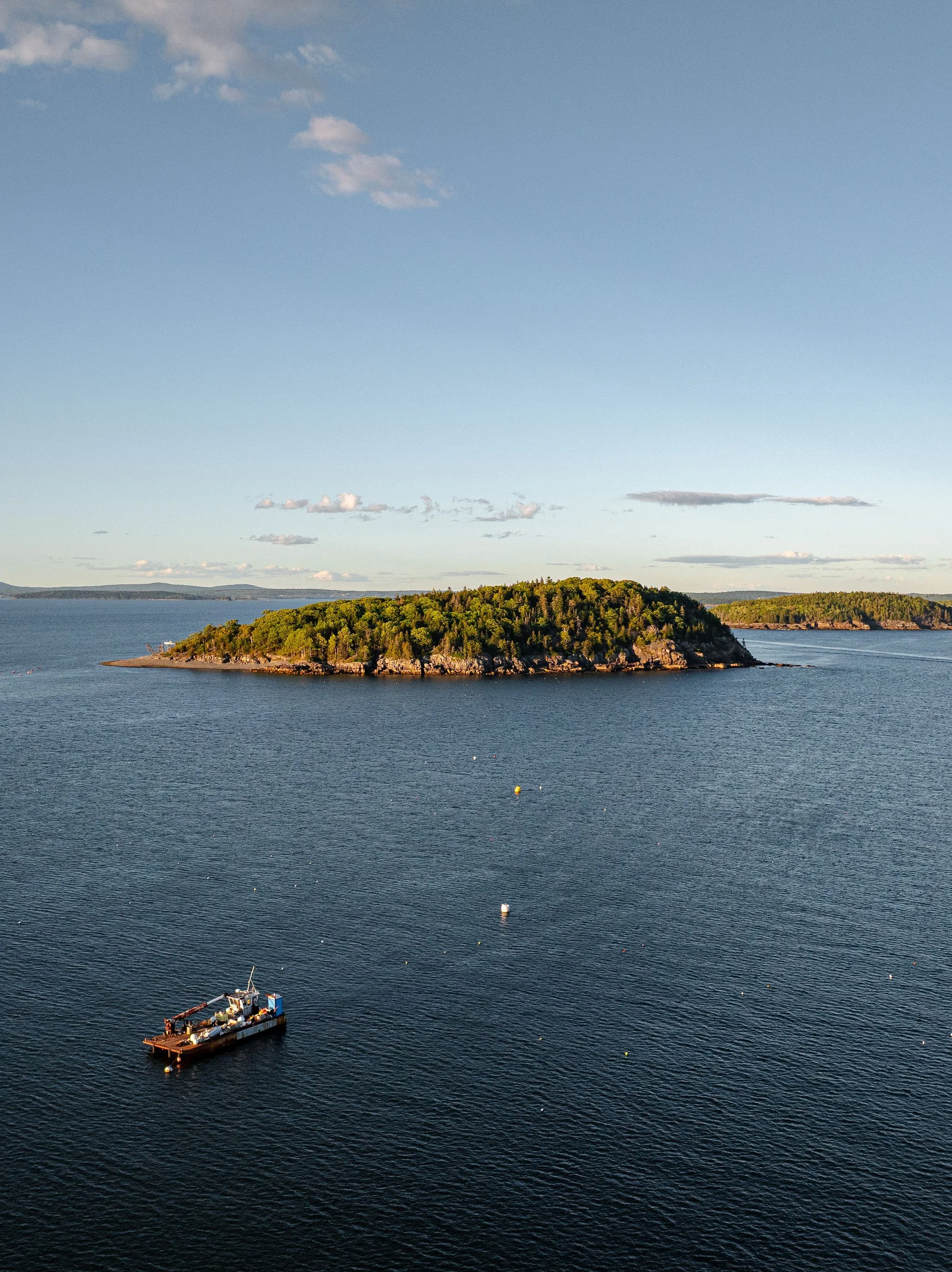 A small boat floating on calm water near a hilly, tree-covered island under a clear sky.