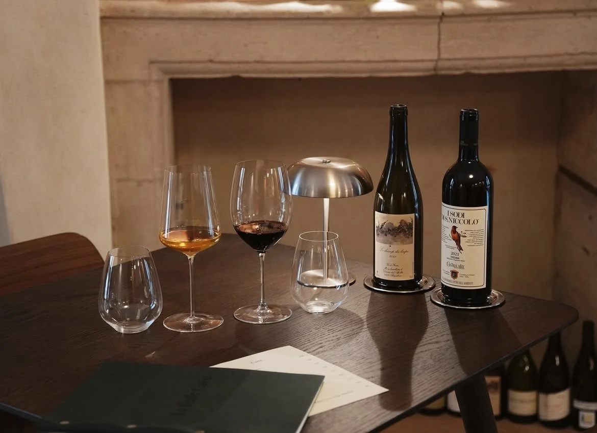 Verres de vin rouge et rosé, deux bouteilles de vin, une lampe de table en acier sur une table en bois.