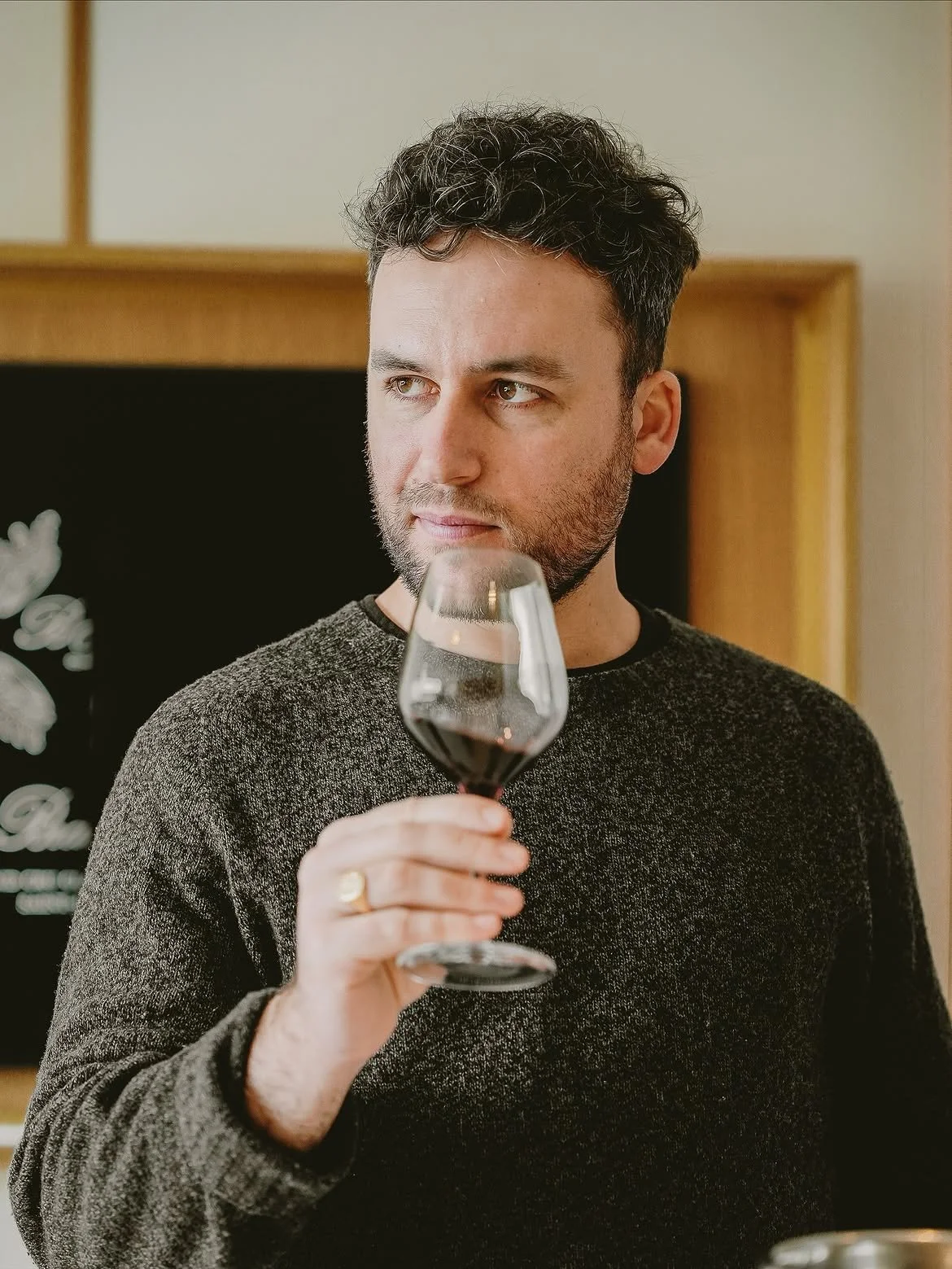 Un homme tient un verre de vin rouge, regardant à droite.