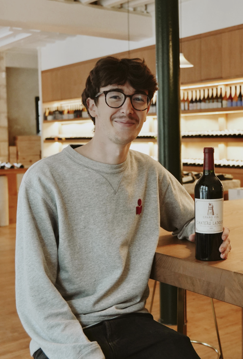 Jeune homme avec lunettes souriant, tenant une bouteille de vin rouge dans un bar ou un restaurant
