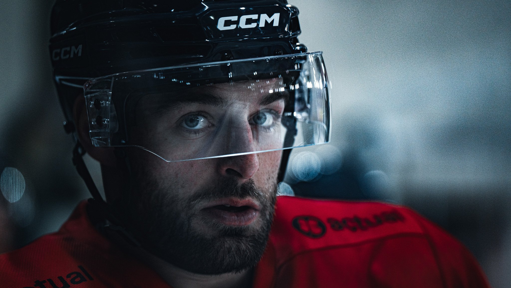 Un joueur de hockey en tenue rouge portant un casque noir avec une visière transparente, regardant fixement.