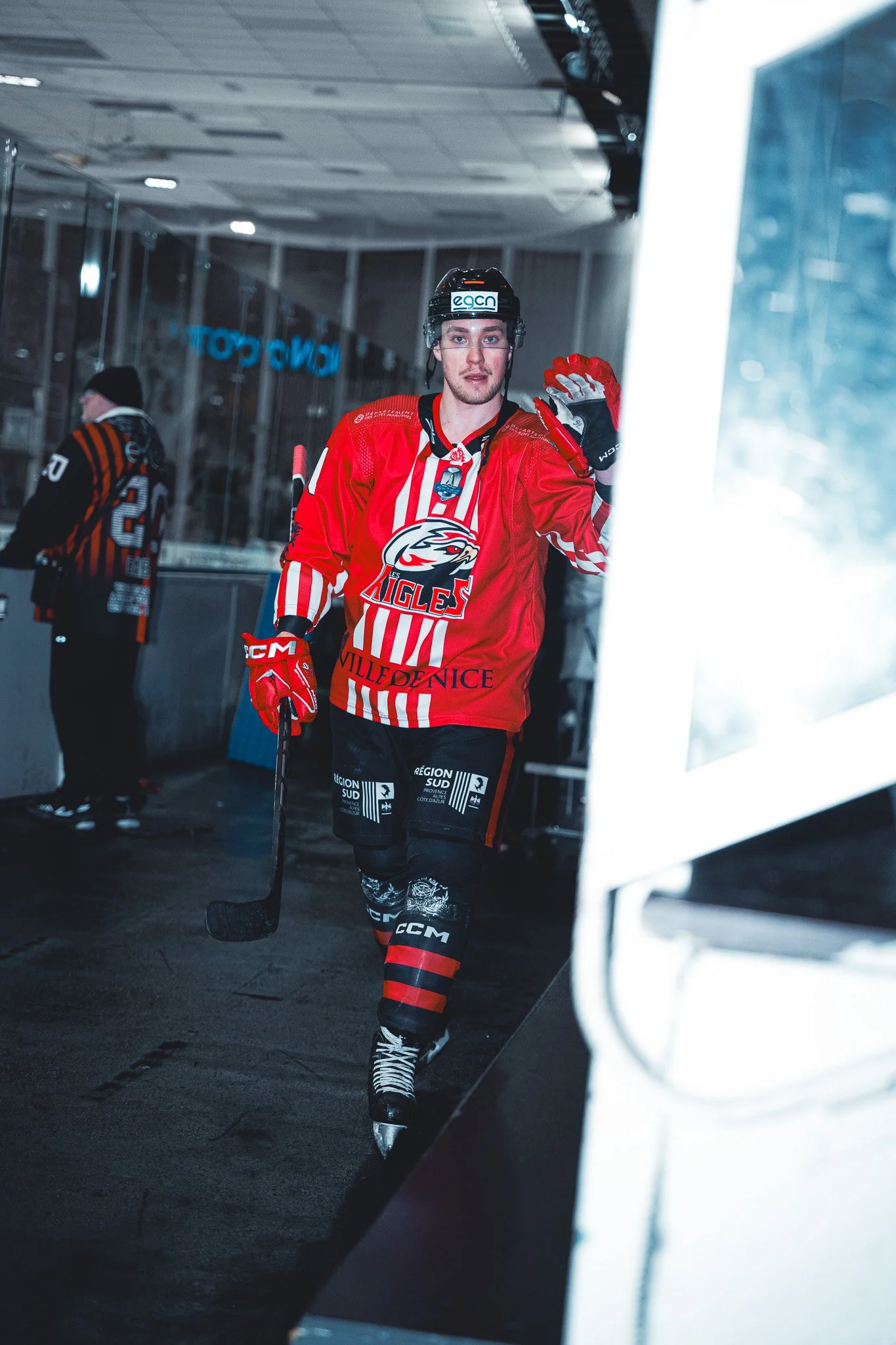 Joueur de hockey sur glace en tenue rouge dans un vestiaire, tenant un bâton de hockey.