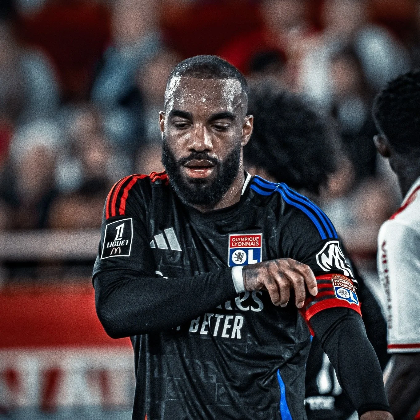 Un joueur de football portant le maillot noir de l'Olympique Lyonnais, qui ajuste son maillot avec sa main gauche, sur un terrain de football.