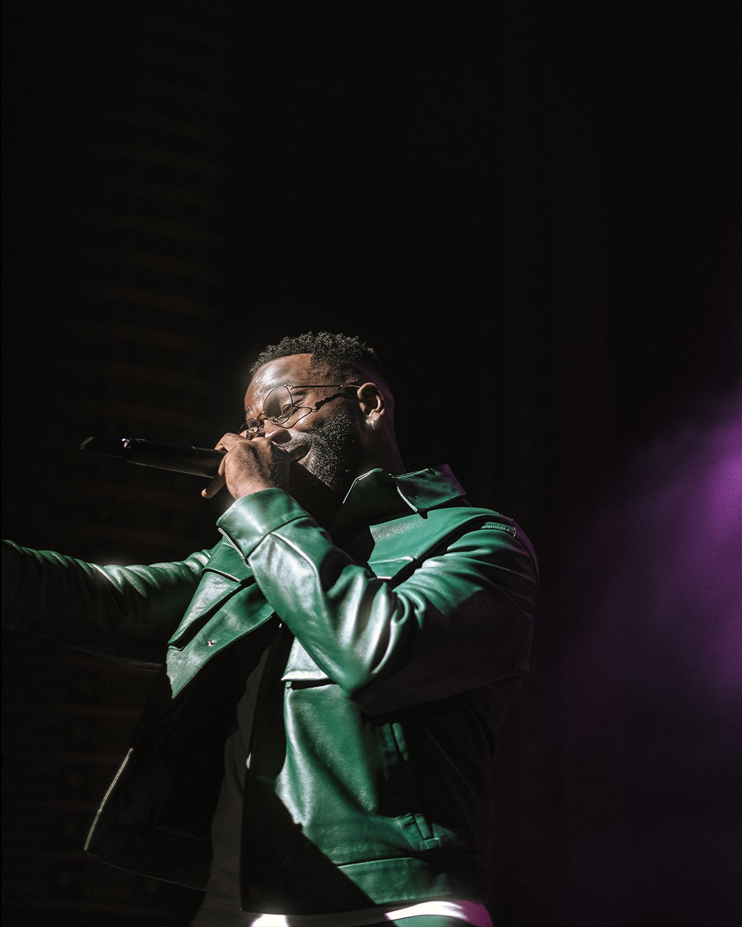 Homme en veste verte chantant sur scène avec un microphone.