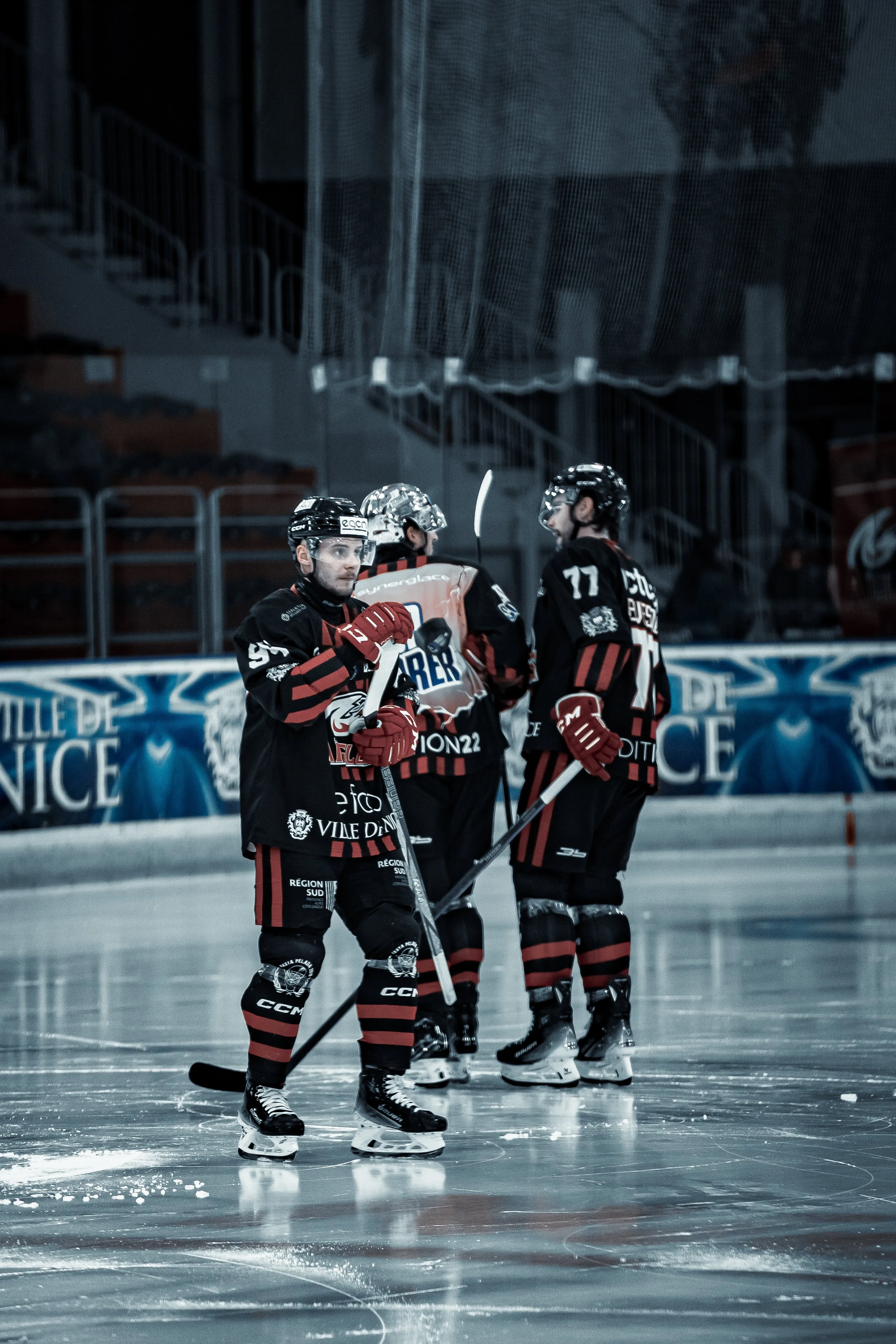 Des joueurs de hockey sur glace en tenue noire et rouge avec des bâtons sur une patinoire.