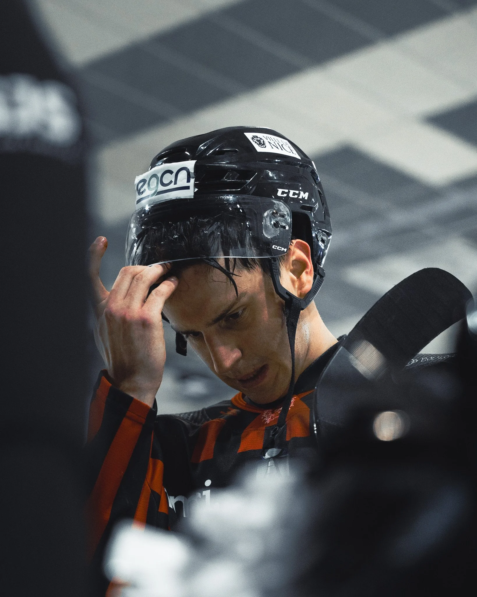 Joueur de hockey portant un casque noir et un maillot rayé rouge et noir, tenant son casque en ajustant sa sangle.