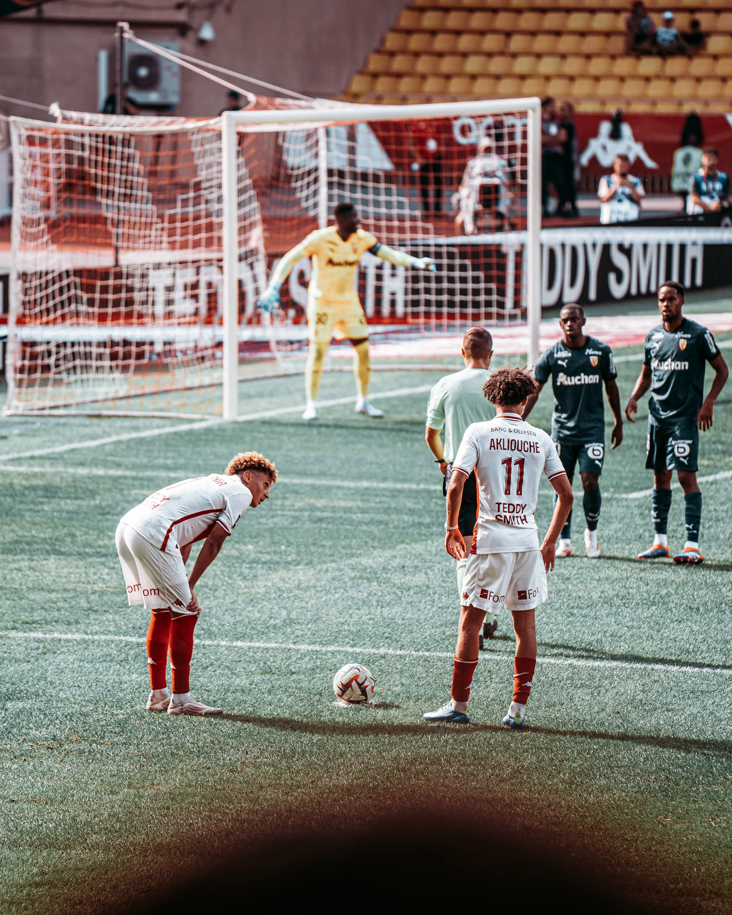 Joueurs de football se préparant pour un coup franc sur un terrain de football, un gardien en tenue jaune dans le but.