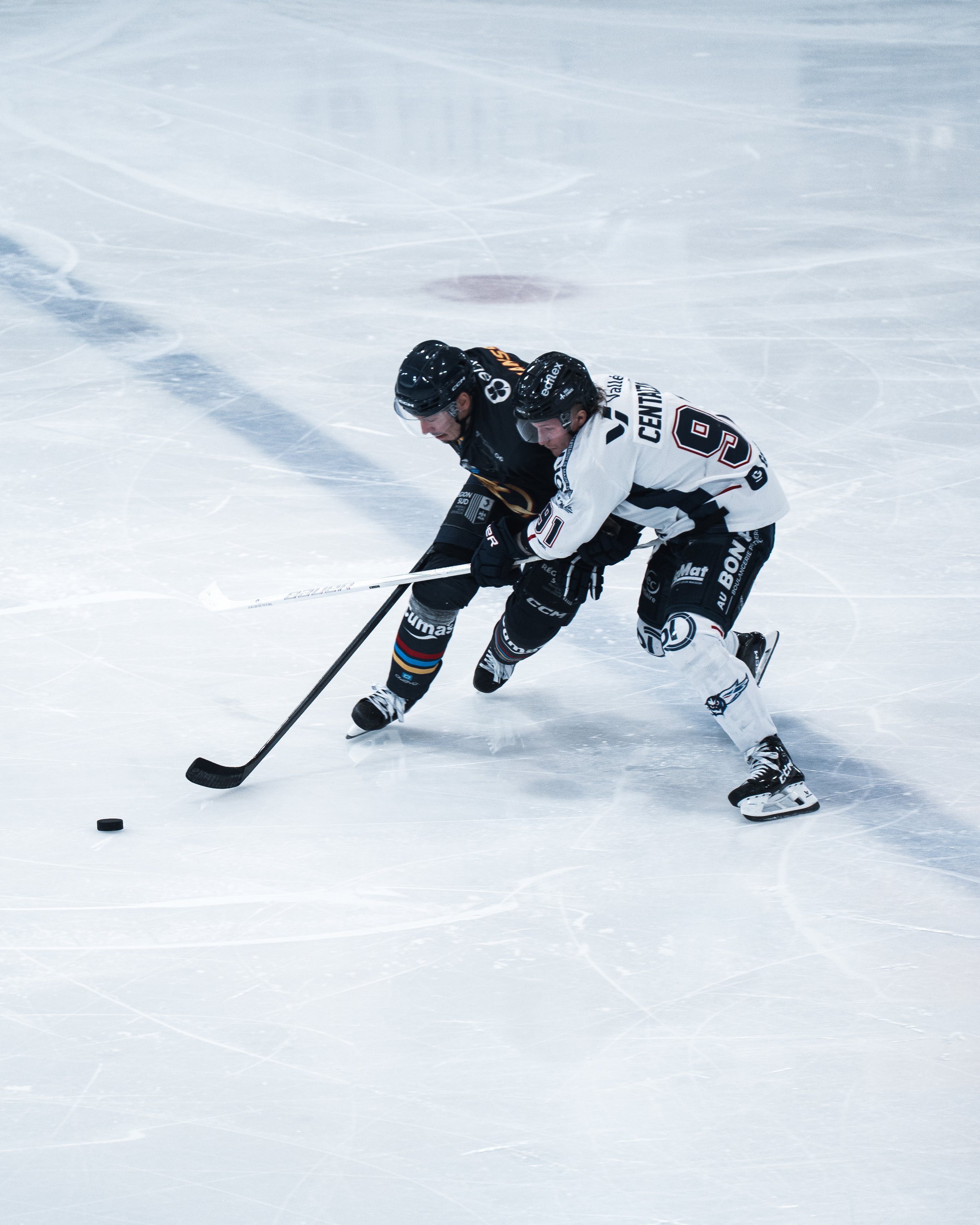 Deux joueurs de hockey en compétition sur la glace, l'un en noir et l'autre en blanc, essayent de prendre ou de contrôler la rondelle.