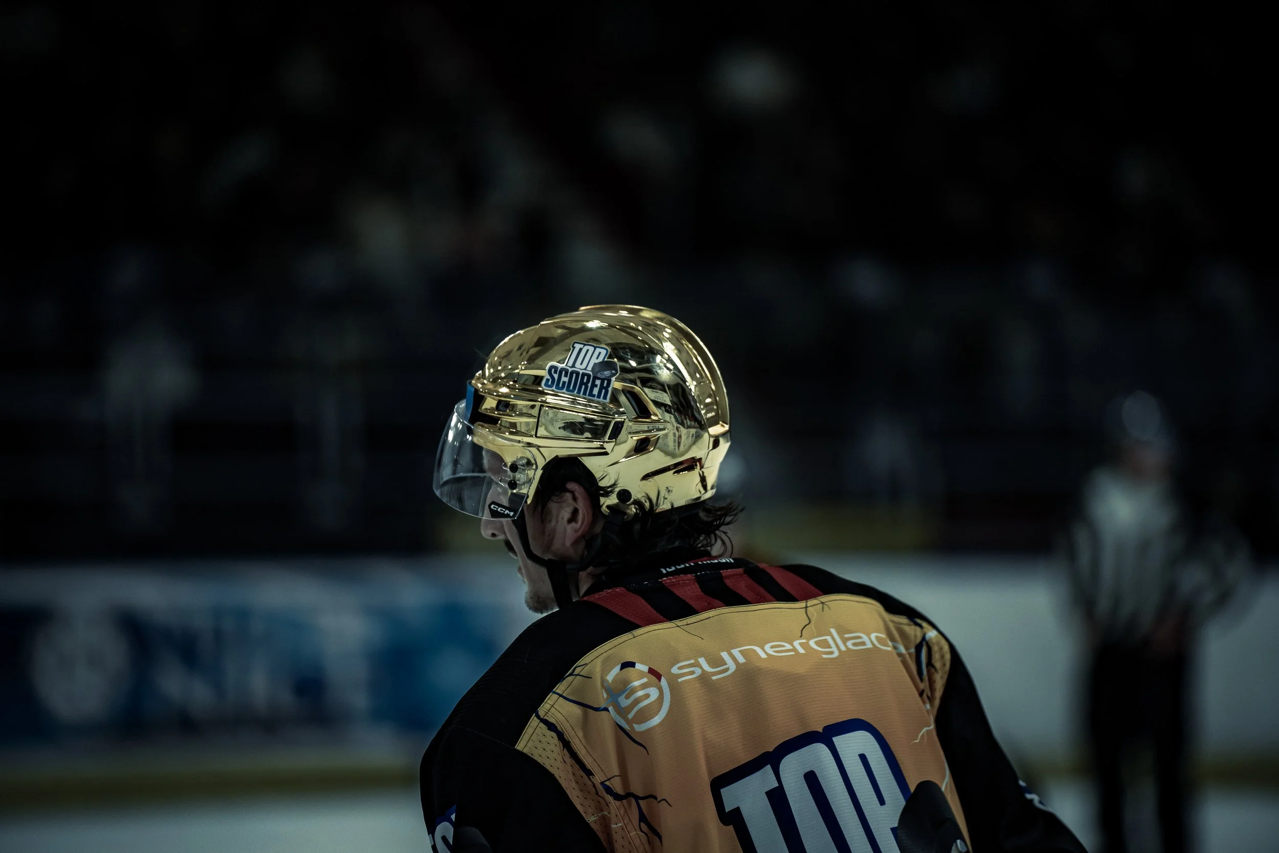 Joueur de hockey sur glace avec un casque doré marqué "TOP SCORER" sur la glace.