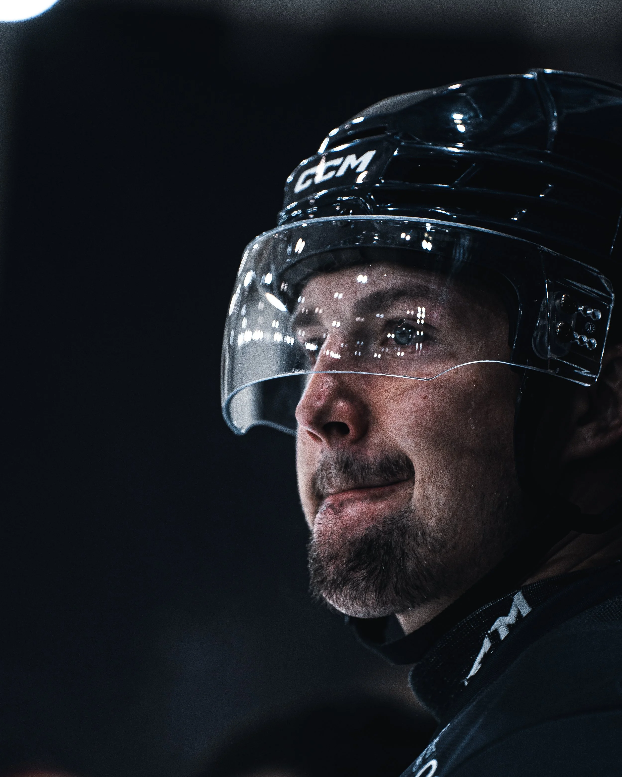 Homme portant un casque de hockey avec visière, regardant vers l'avant dans un éclairage sombre.