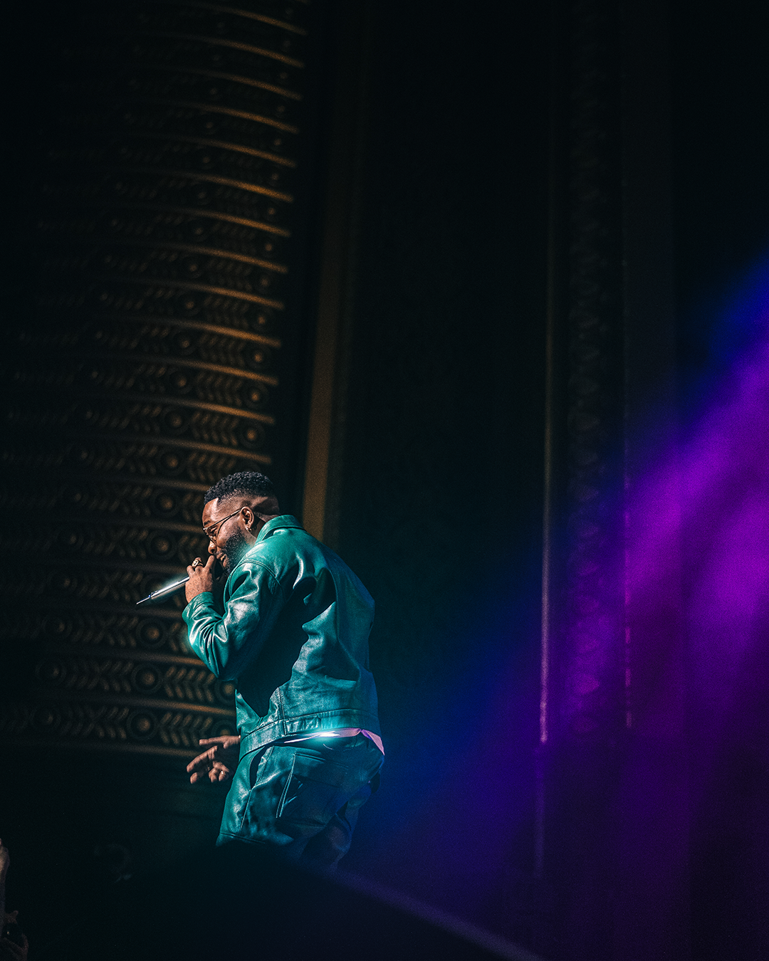 Un chanteur en tenue verte sur scène avec un micro, éclairé par des lumières colorées.