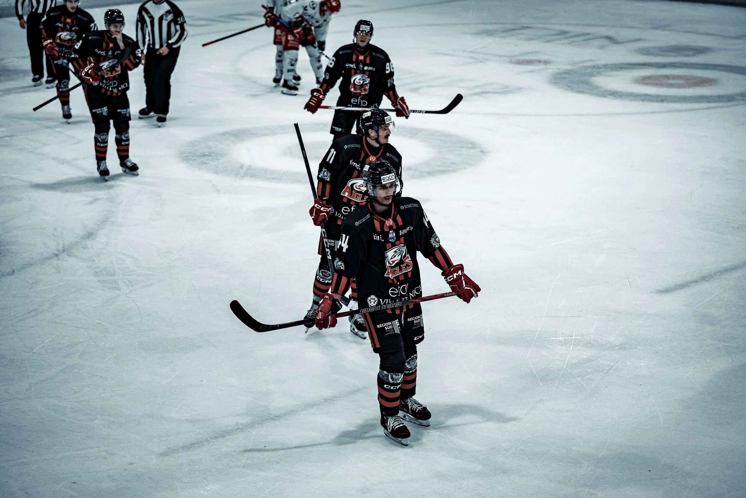 Joueurs de hockey sur glace sur la patinoire, vêtus de maillots noirs et rouges, tenant des crosses de hockey.
