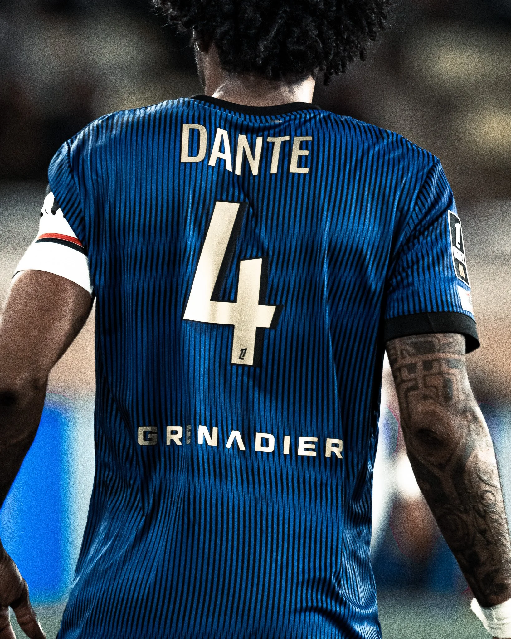 Un joueur de football vu de dos portant un maillot bleu avec le nom 'DANTE' et le numéro 4, avec le mot 'GRANDIER' en dessous.