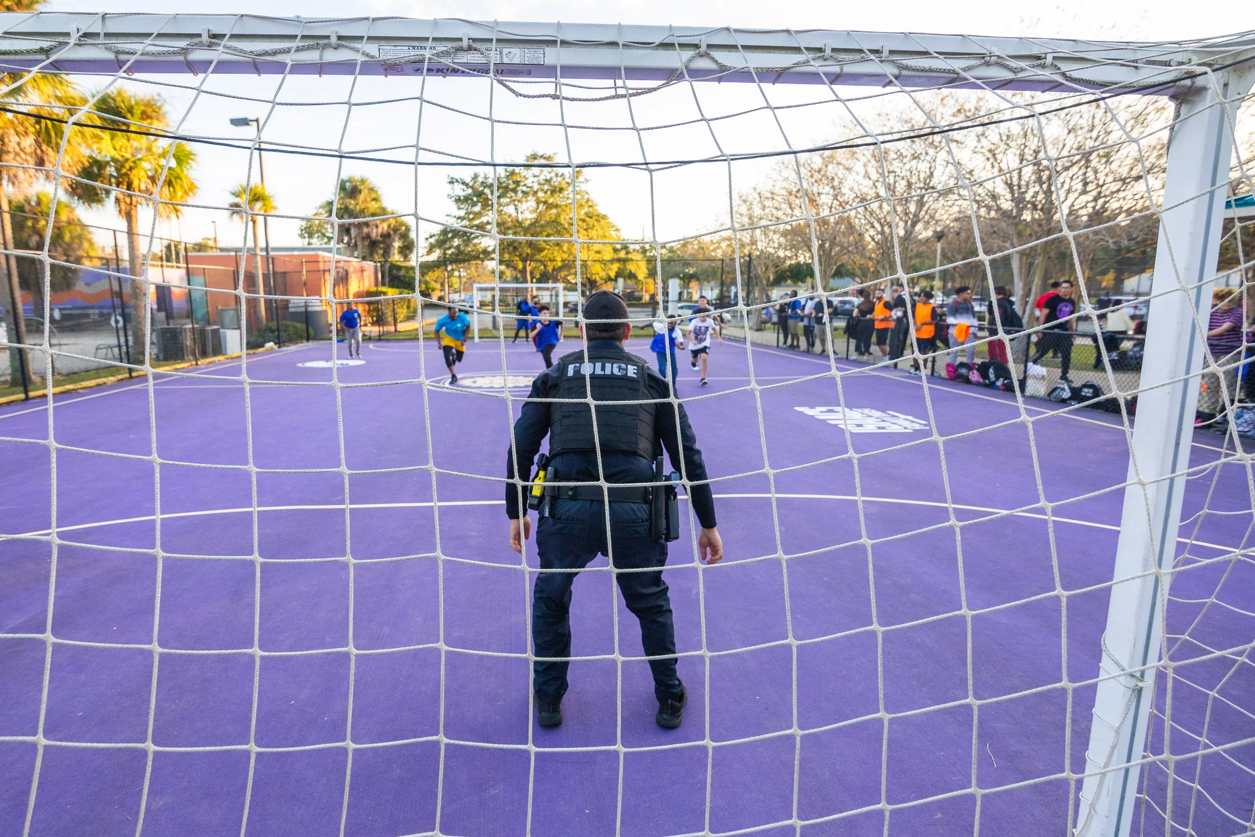 a police officer standing in front of a soccer goal playing soccer with a group of children