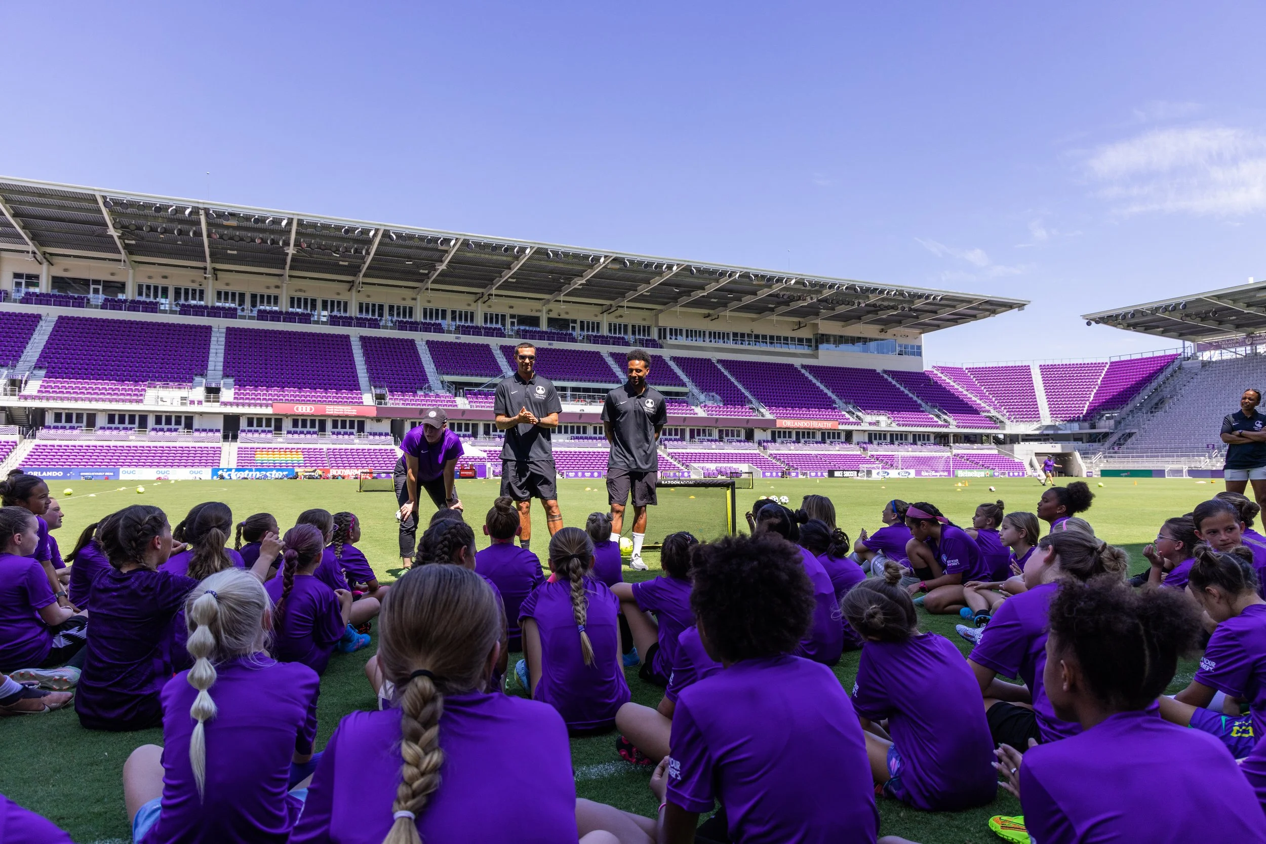 a group of soccer coaches are talking to a group of young female soccer players at the stadium after a soccer clinic