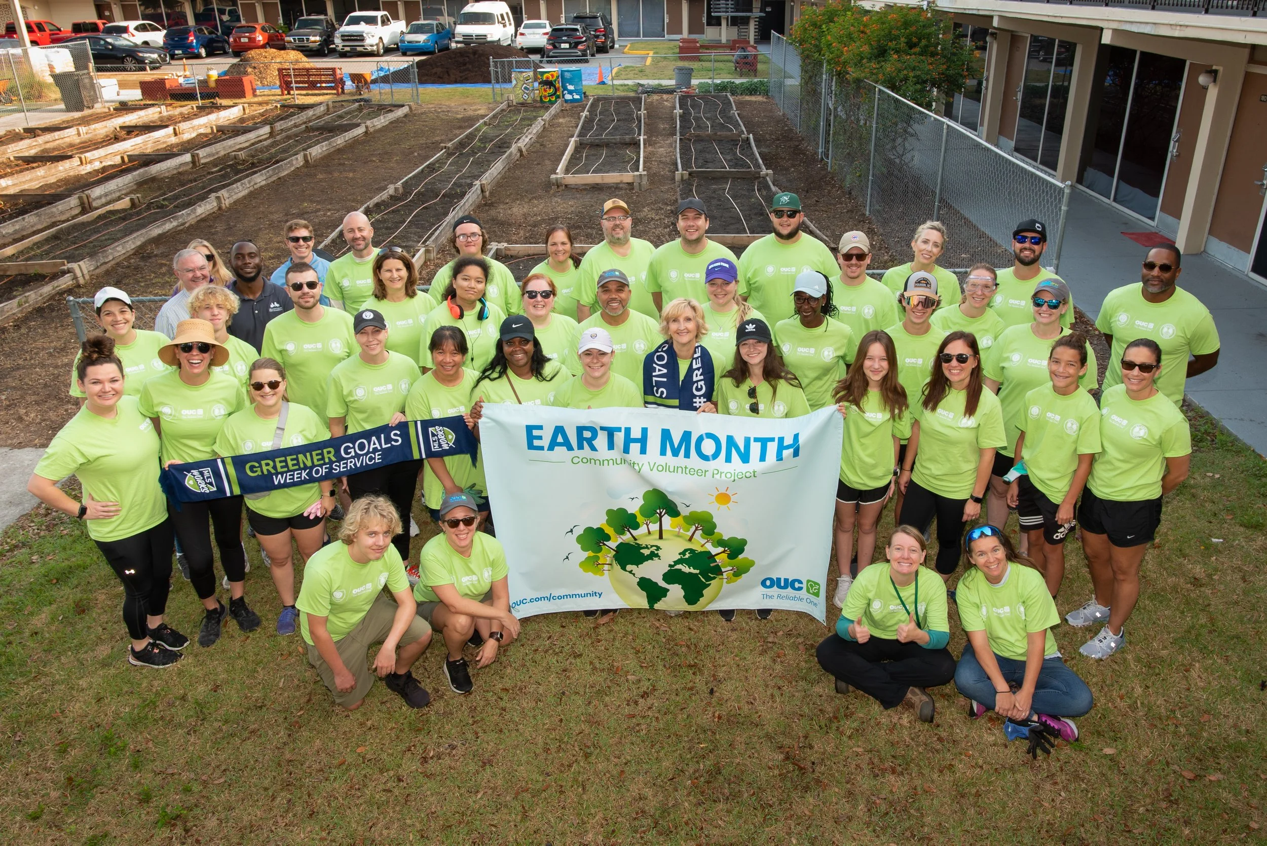 a group of volunteers holding an Earth Day banner in front of several garden beds