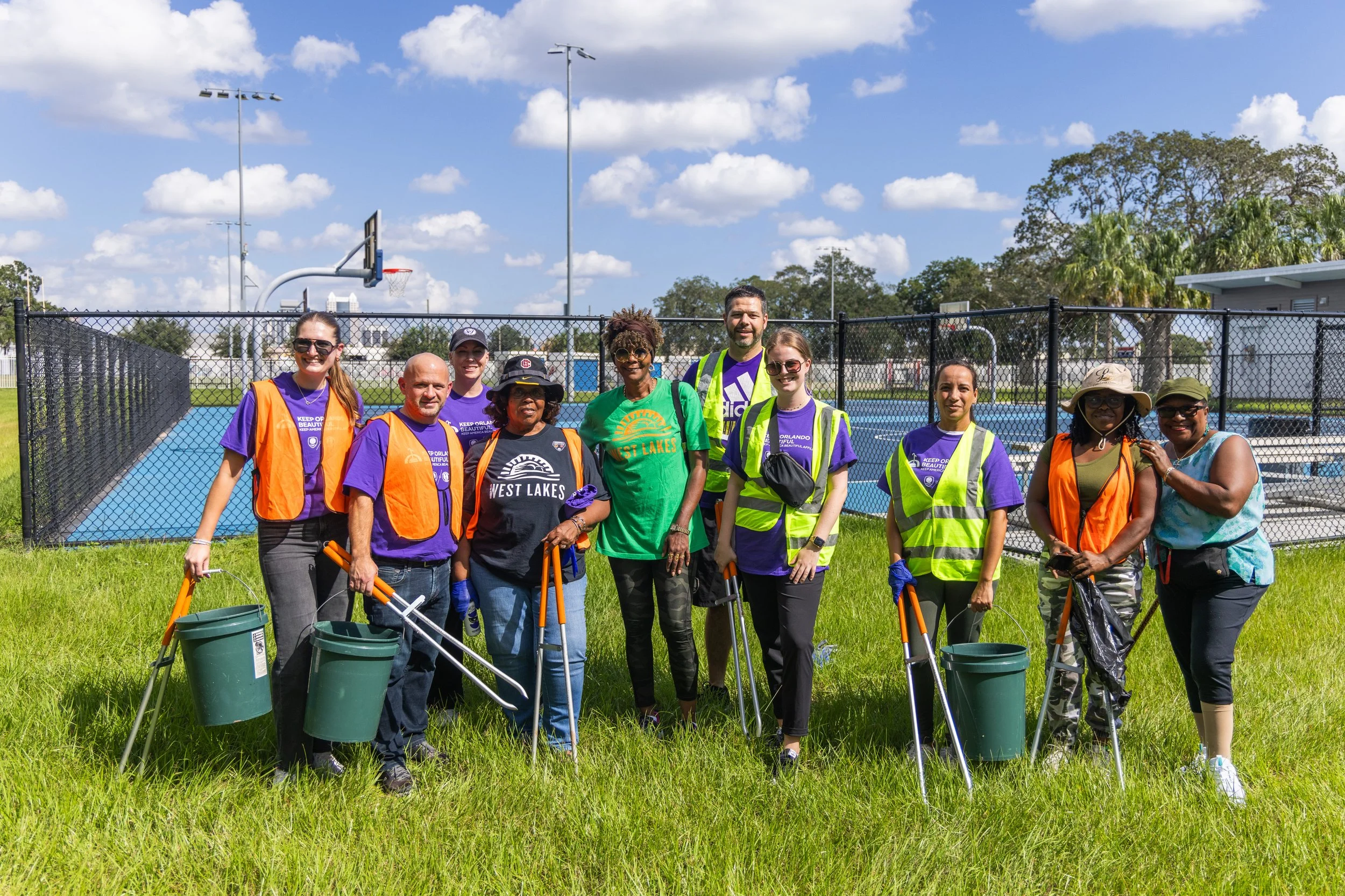 a group of 10 volunteers with fluorescent vests on holdings metal pickers and buckets to collect trash at a volunteer project